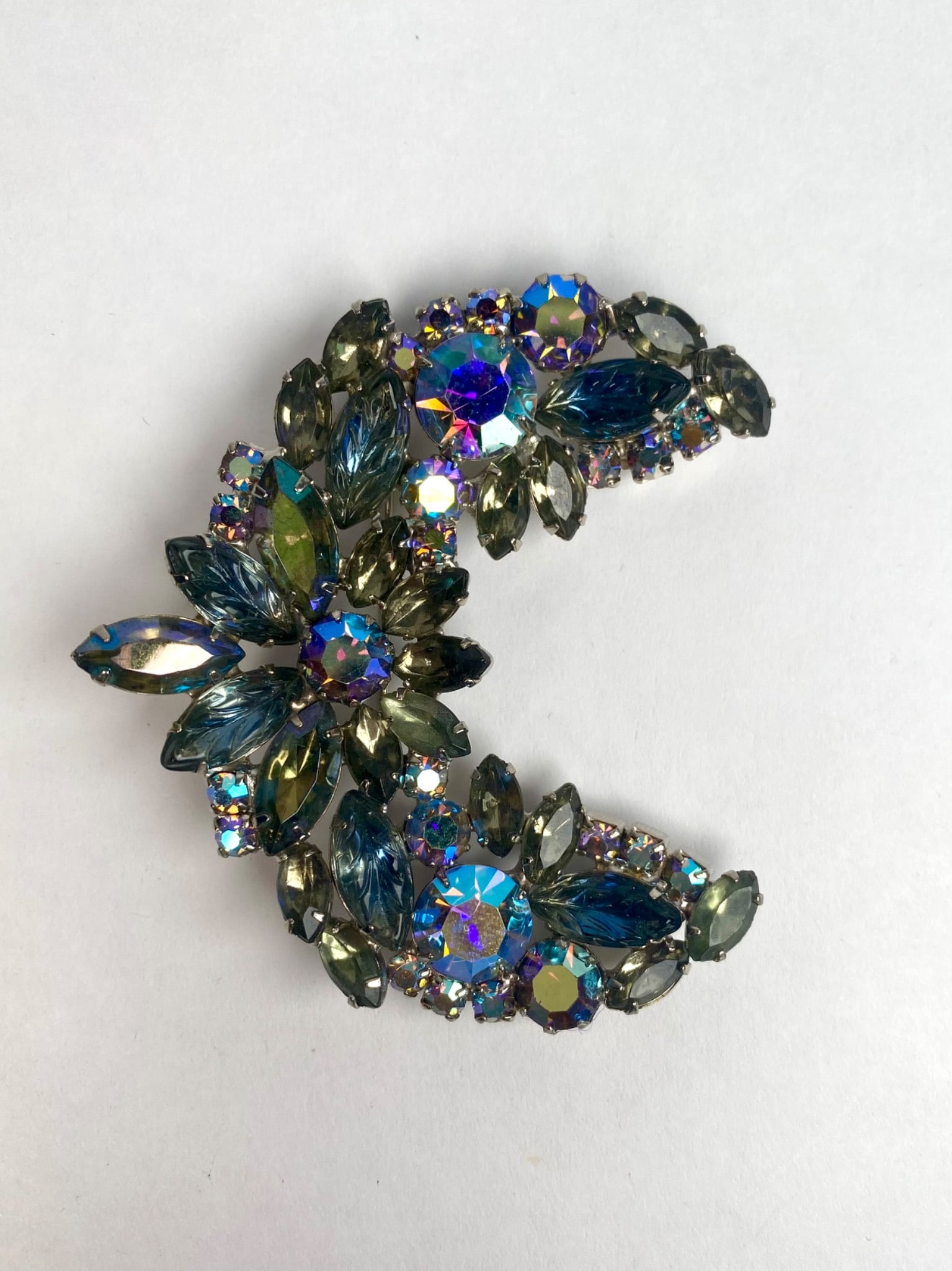 Mid Century Silver Tone and Blue Rhinestone Crescent Brooch: Vintage mid century rhinestone brooch in a distinctive crescent shape. It features a dazzling mix of navette and round cut stones in a blue, aqua and iridescent hues, all prong set in a siler tone set