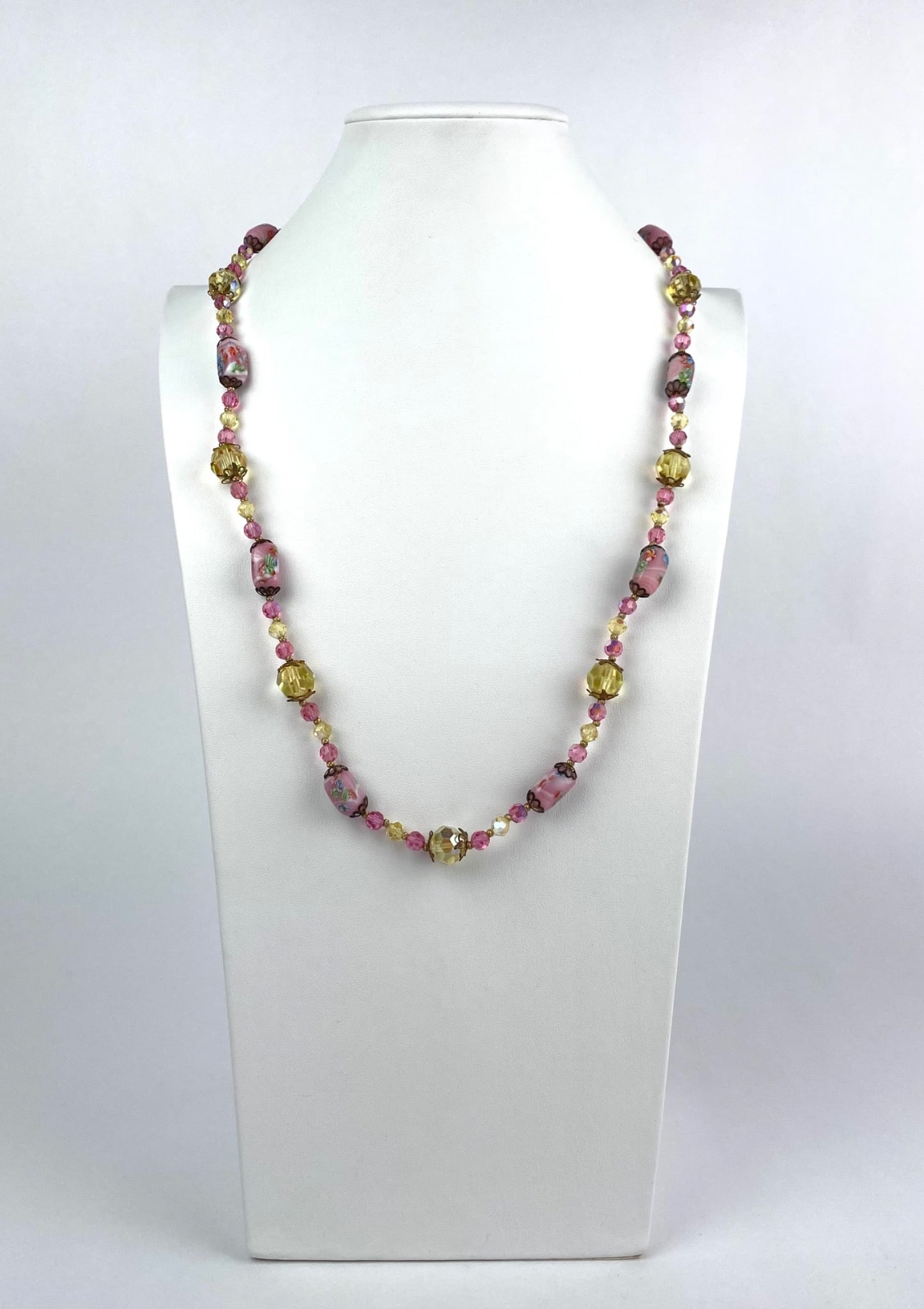 Wedding Cake Beaded Necklace With Pink, Yellow, and Floral Motif: Glass bead necklace featuring an arrangement of pink and yellow beads with floral motif decorations on select beads. Includes a clasp for fastening. The beads exhibit intricate detailing and alternati