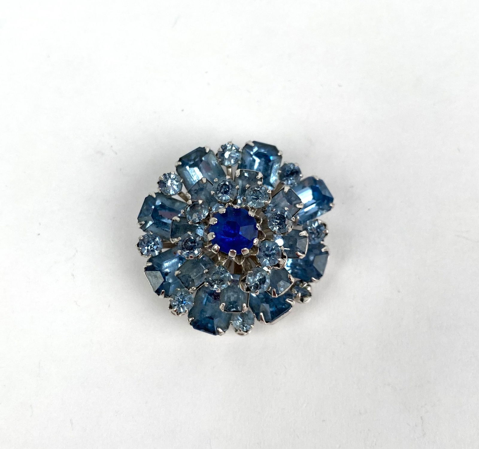 Coro Silver Toned Brooch with Blue Stones, Marked and Multi Tiered: Silver toned brooch featuring multi-tiered construction with a central dark blue stone surrounded by lighter blue stones in varying cuts and sizes. The reverse shows a secure pin mechanism and a maker