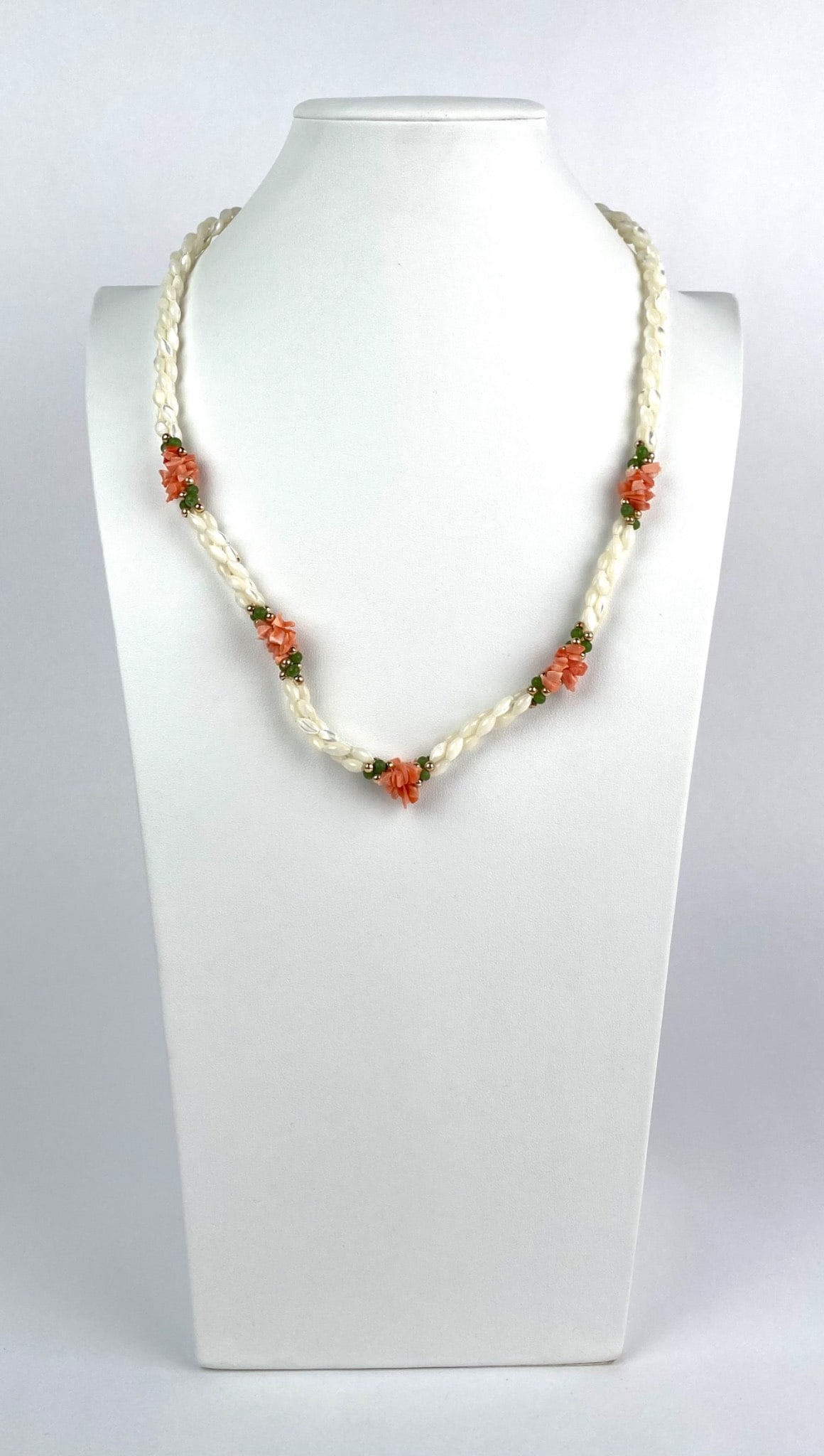 Pearl and Coral Bead Necklace with Gold Tone Clasp: Pearl and coral bead necklace featuring twisted strands of pearlized beads adorned with clusters of orange coral and green accent beads, fastened with a gold tone hook clasp. Dimensions Approx. 11 inc