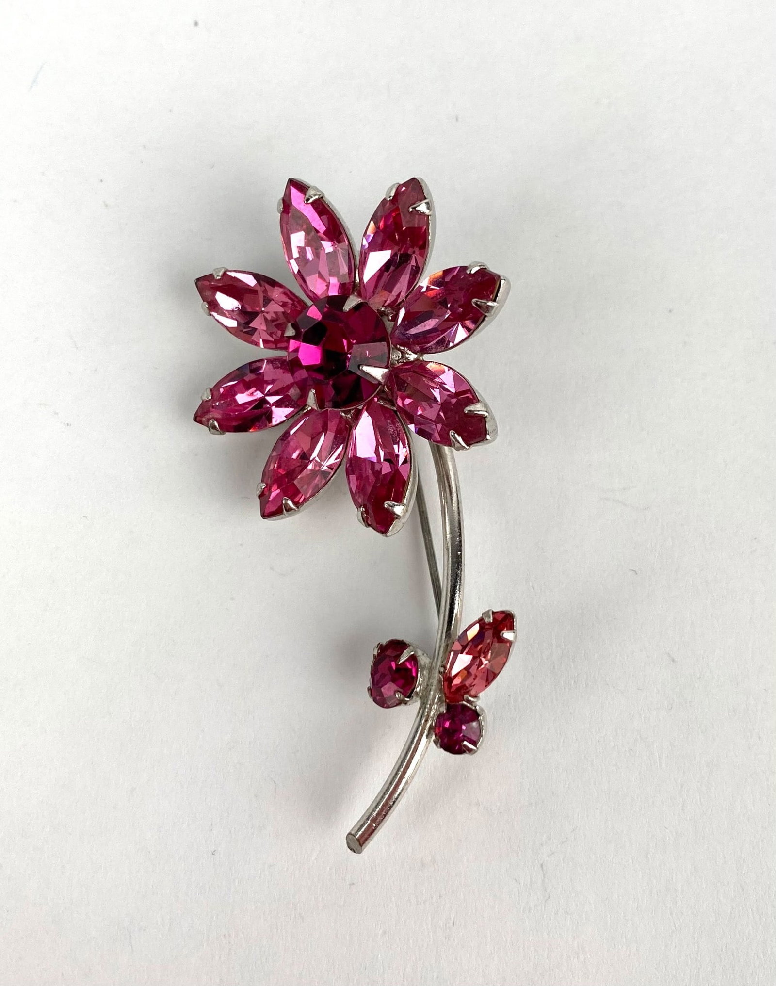 Reed and Barton Pink Rhinestone Flower Brooch in Silver-Tone Setting: Reed and Barton flower brooch featuring pink rhinestone petals and a central pink rhinestone in a silver tone metal setting. The brooch is designed with a curved stem adorned with two additional rhine