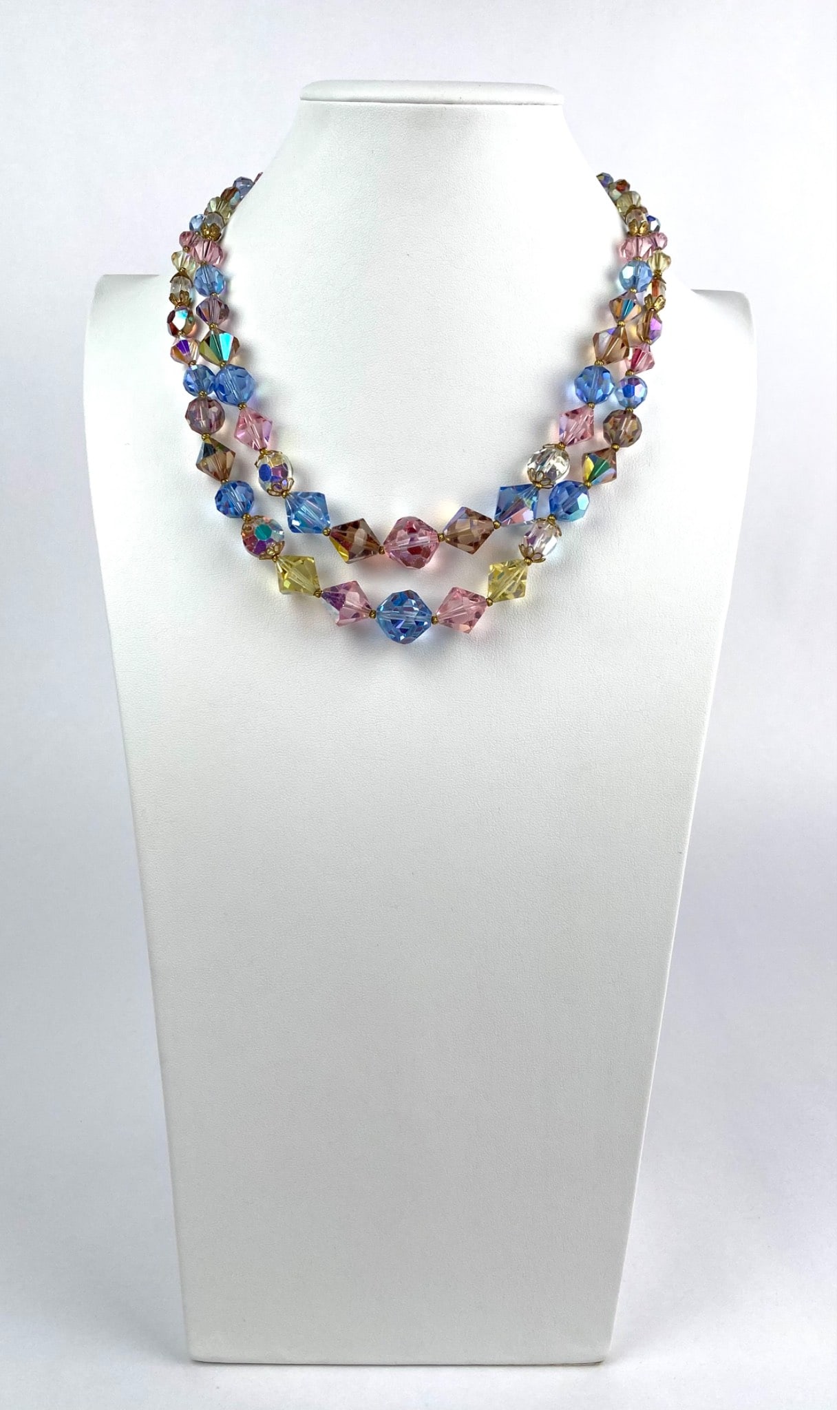 Double Strand Multicolor Faceted Crystal Necklace: Double strand necklace composed of multicolor faceted crystal beads in pink, blue, yellow, and clear hues. Features a detailed gold tone floral clasp. Condition shows wear commensurate with age and us
