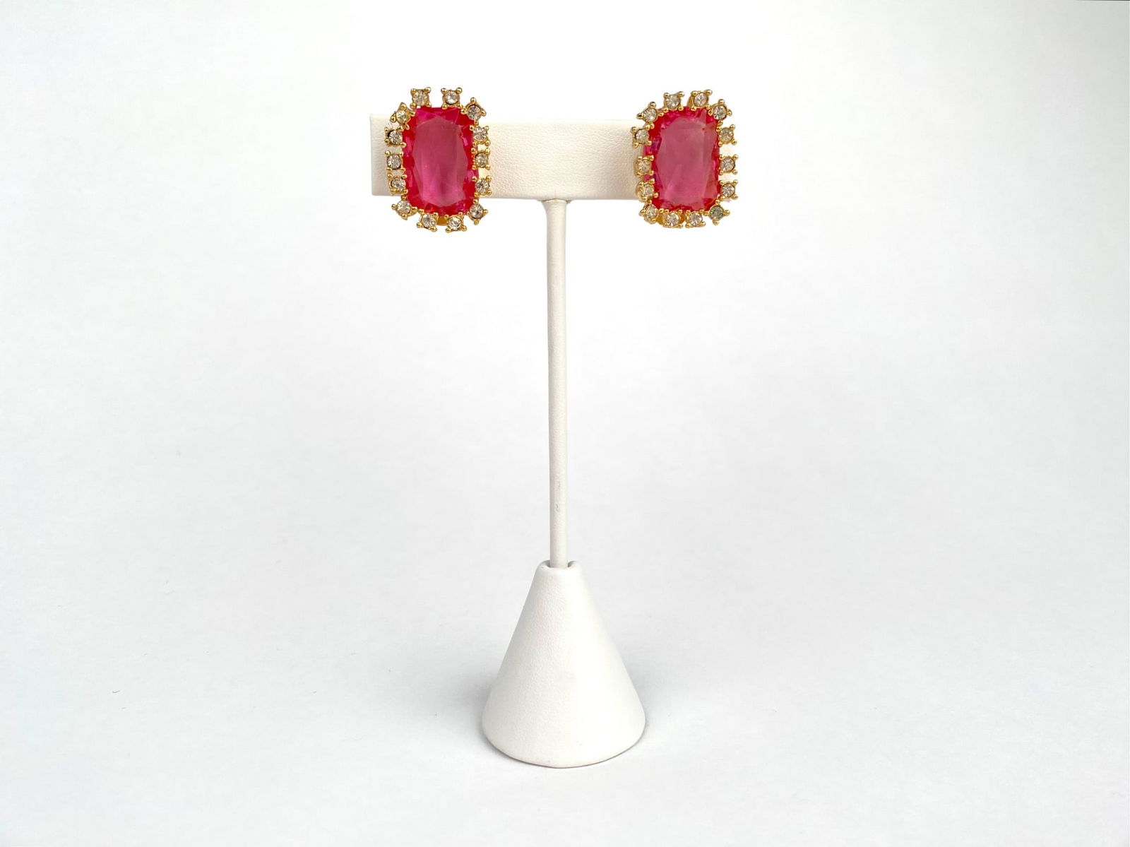 Vintage Hattie Carnegie Clip on Earrings with Pink Stones: Pair of Hattie Carnegie yellow gold tone clip on earrings featuring rectangular pink central stones surrounded by clear stone accents, designed in an ornate setting. Stamped on the back of each clip f