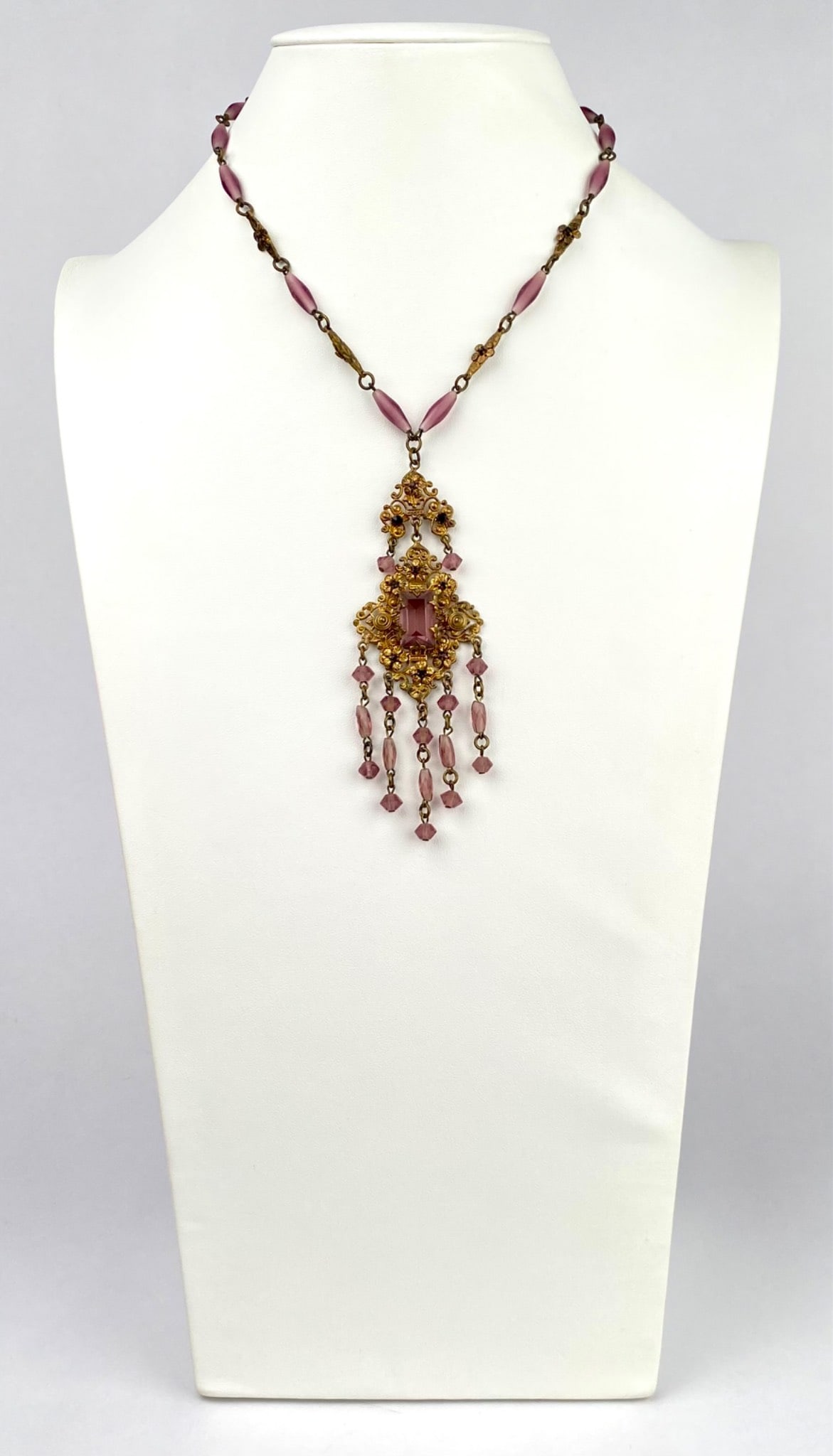Czech Art Nouveau Gold Tone Necklace With Purple Glass Beads: Gold tone necklace featuring a prominent pendant showcasing intricate filigree work and purple glass beads. The pendant includes dangle elements with coordinated purple beads, enhancing its decorative