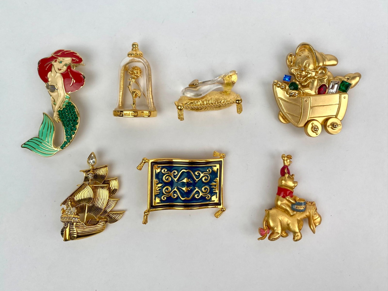 Lot of Seven Disney Character Gold Tone Brooches: Set of seven Disney themed gold tone enamel brooches featuring beloved characters and scenes, including Ariel (The Little Mermaid), the enchanted rose from Beauty and the Beast under a clear dome, Cin