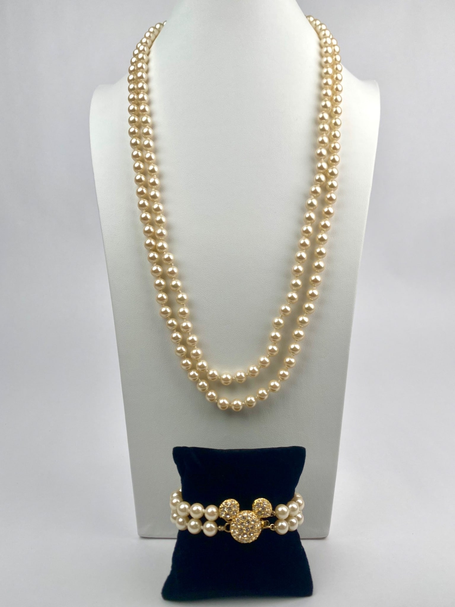 Disney Pearl Necklace and Bracelet Set Featuring Rhinestone Clasp: Disney branded jewelry set including a double strand faux pearl necklace and a matching double strand bracelet. Both pieces feature gold tone clasps adorned with rhinestone encrusted Mickey Mouse silh