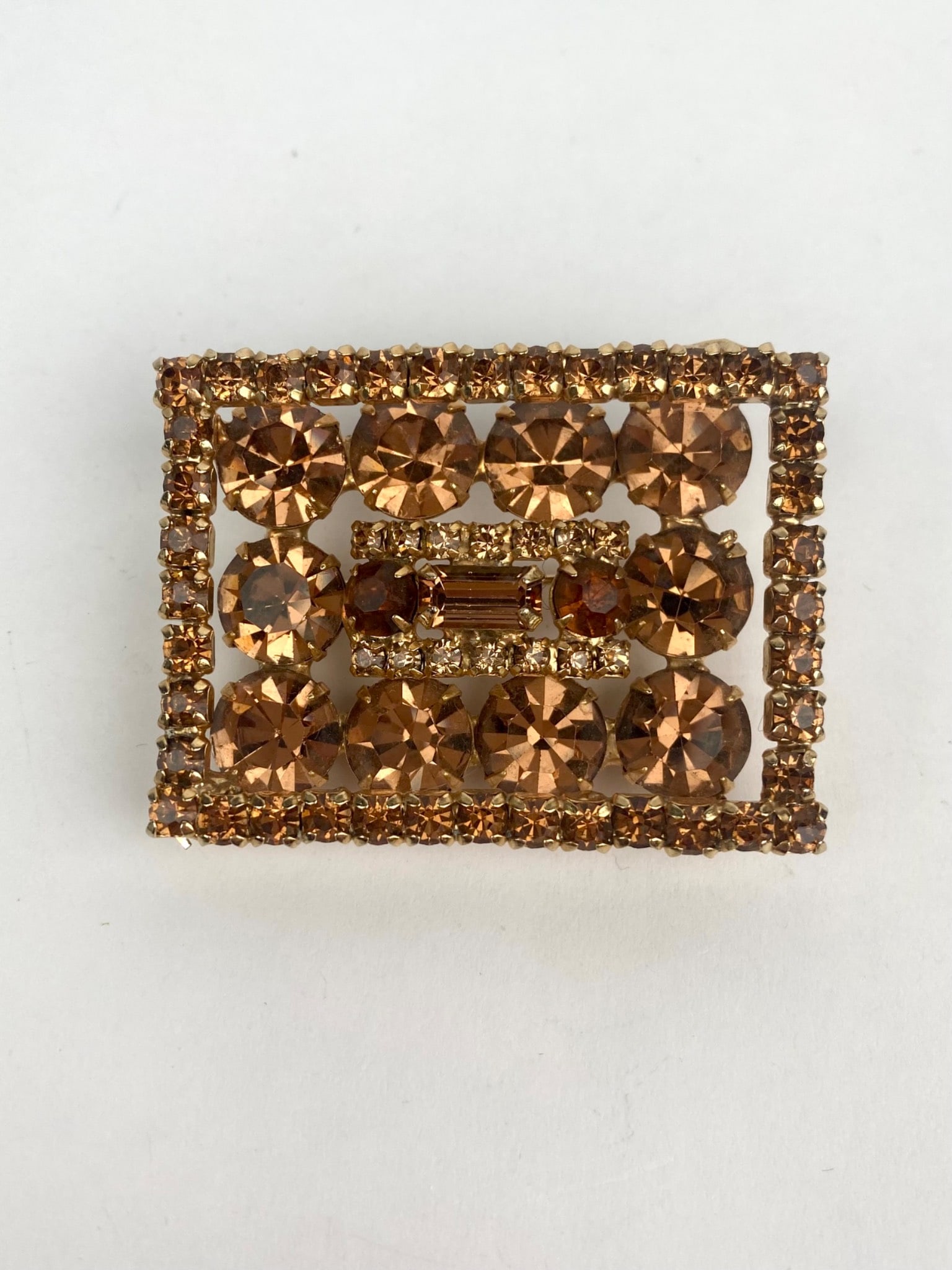 Kramer Mid Century Amber Rhinestone Brooch: Rectangular shaped brooch by Kramer, featuring amber colored rhinestones arranged in an intricate design. The gold tone base is detailed with a secure pin closure on the back, bearing the Kramer mark.