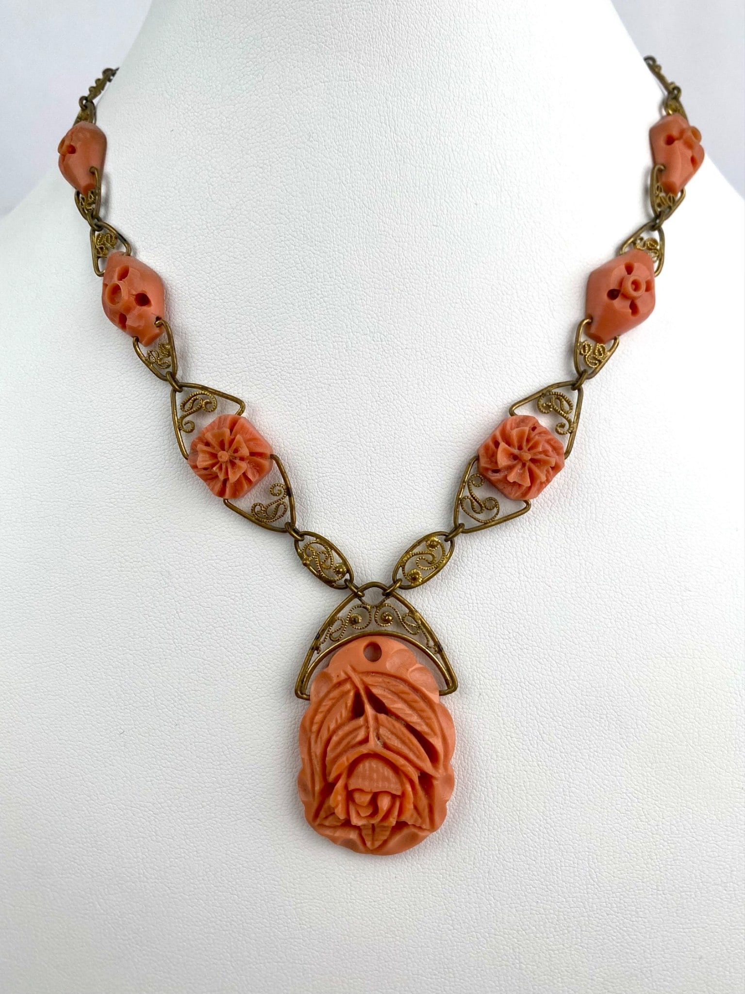 Art Deco Carved Celluloid Floral Necklace with Filigree Brass Links: Art Deco era necklace featuring intricately carved salmon colored celluloid floral elements, including a large central pendant with a dimensional rose design. Smaller flower shaped plaques are intersp