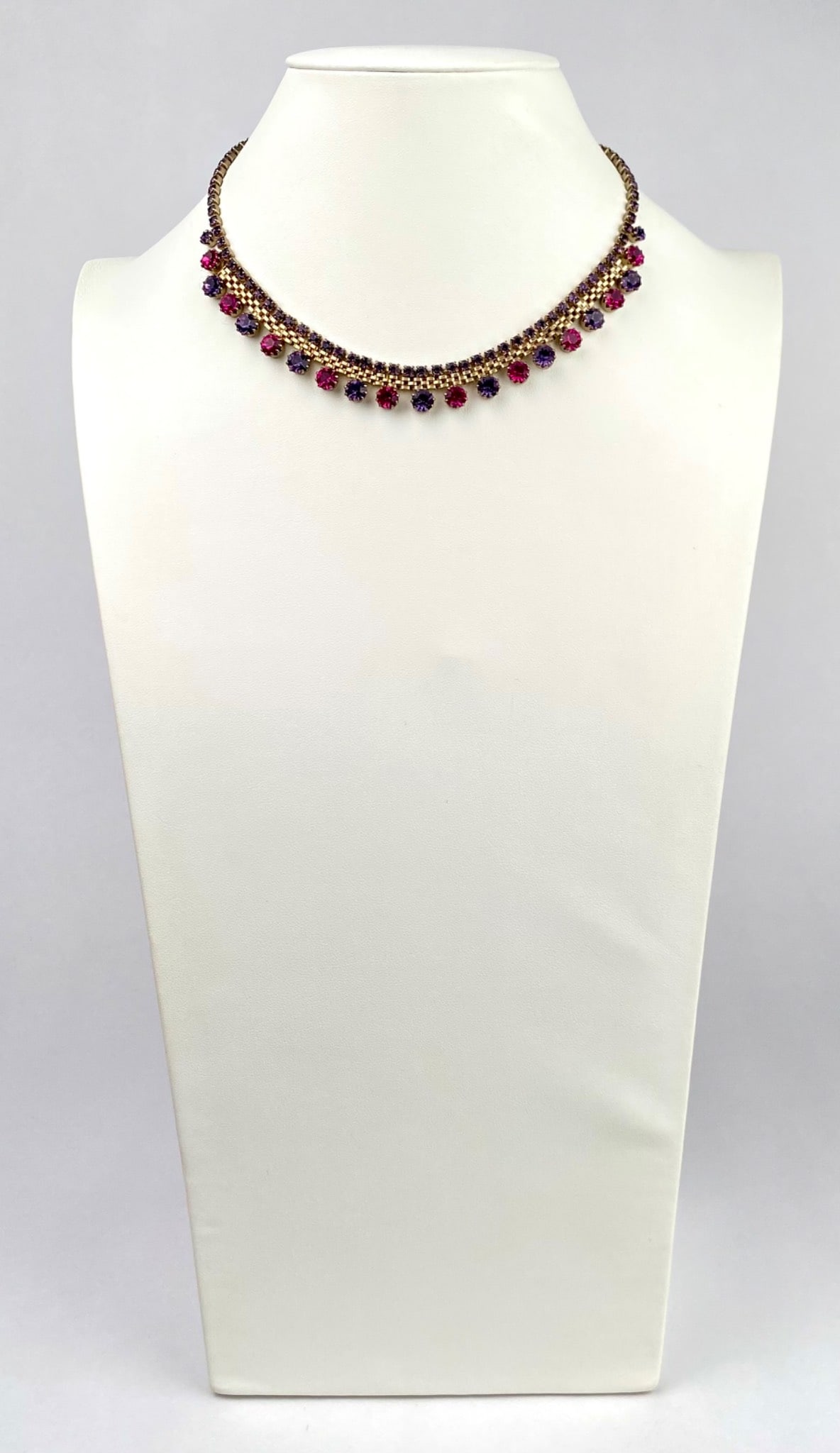 Vintage Rhinestone Choker Necklace in Fuchsia and Amethyst Tones: Gold tone necklace featuring alternating pink and purple rhinestones set in a double row chain design. Decorated with dangling round cut stones in varying shades of pink and purple for added elegance.