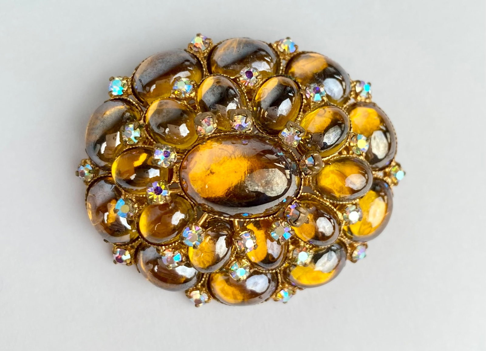 Mid Century TRIAD Amber Glass Cabochon Brooch: Mid Century gold tone brooch with amber colored glass stones in various oval shapes, accented by small iridescent rhinestones. The reverse side includes a pin back closure with a safety clasp. Marked 