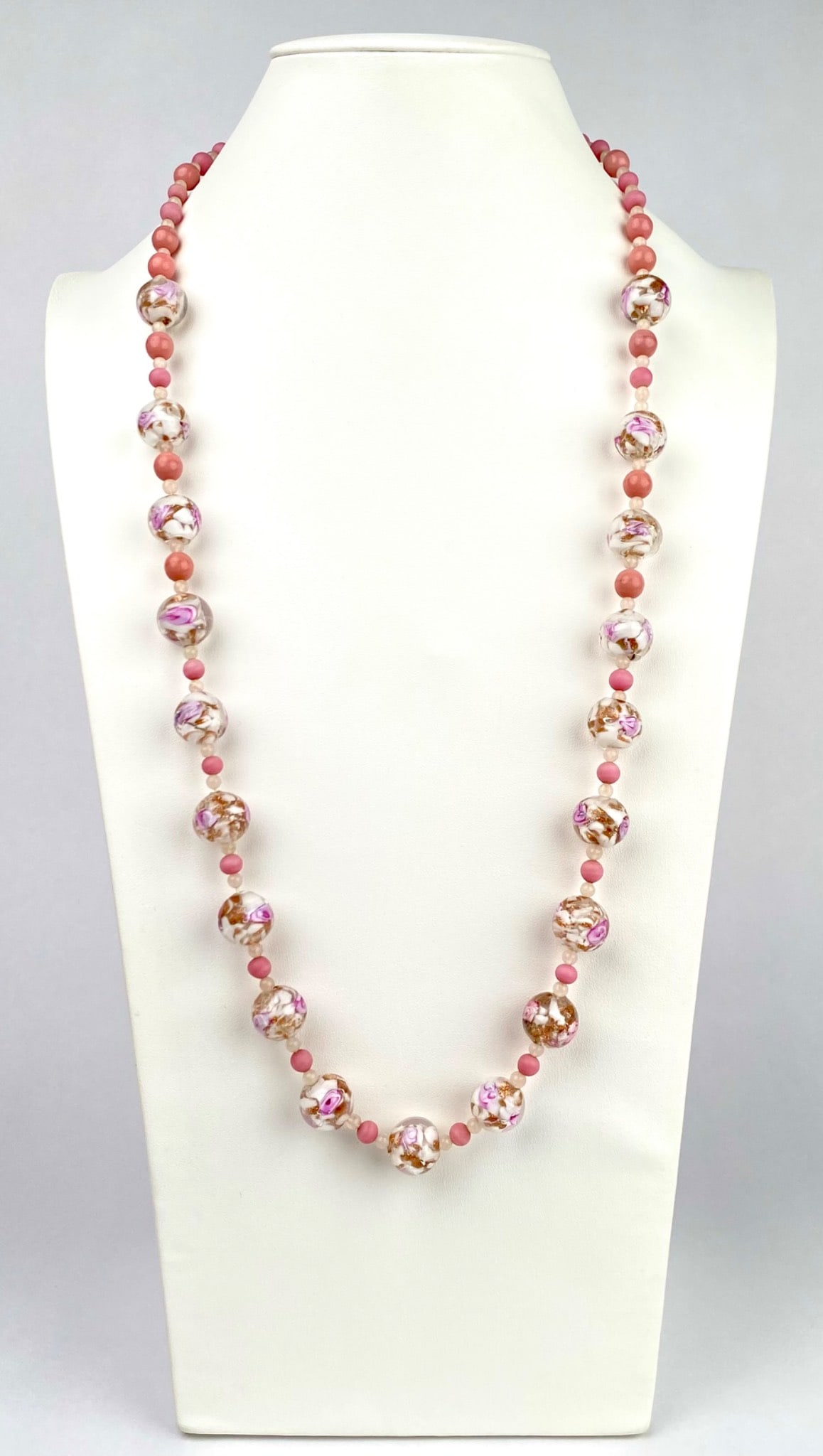 Mid Century Pink Lampwork Floral Bead Necklace (1/20 14K Clasp): This is a vintage beaded necklace featuring smooth, round lampwork glass beads with encased pink and white floral designs, accented by matte pink spacer beads. The floral beads resemble traditional Mu