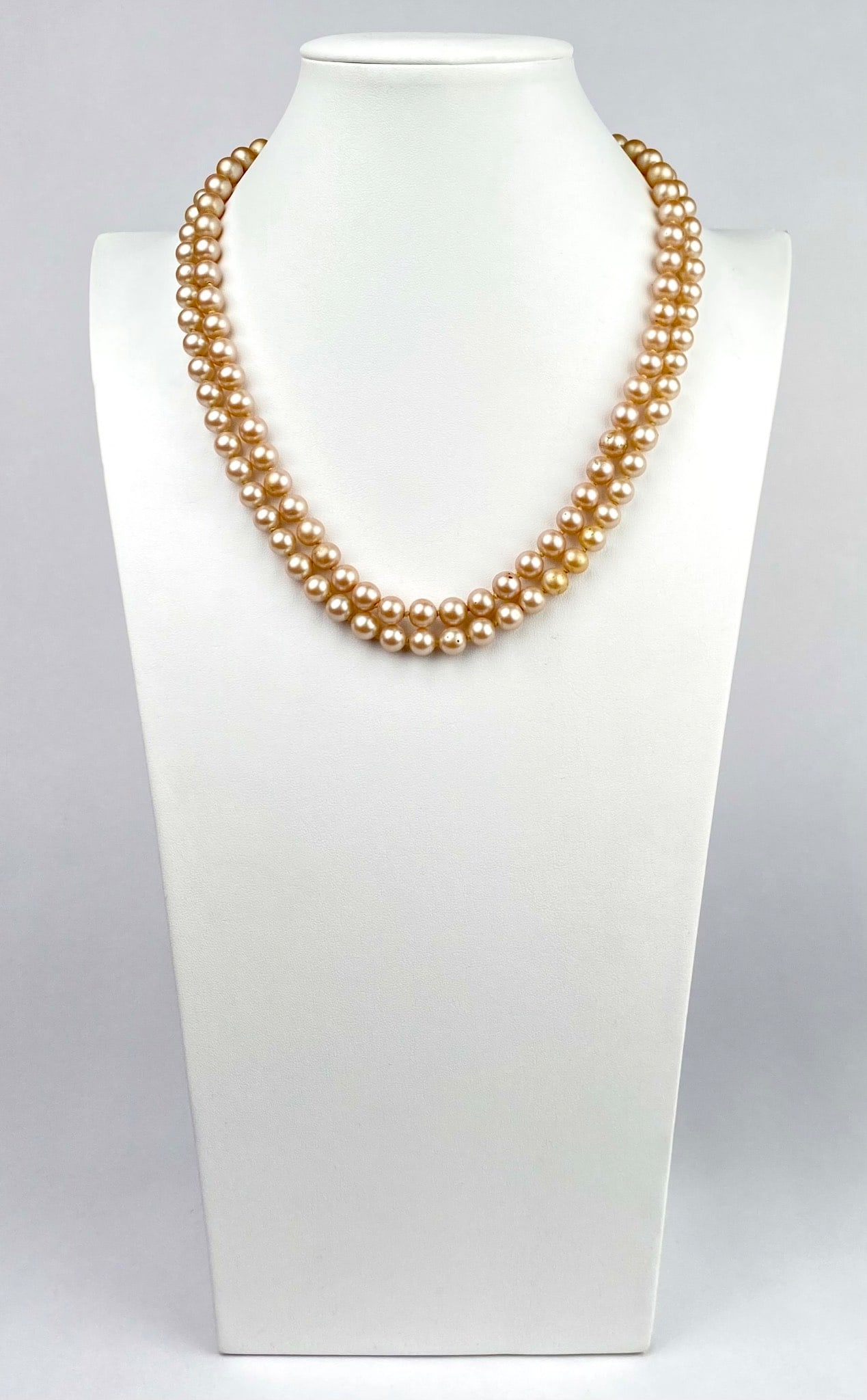 Mid Century Double Strand Champagne Glass Pearl Necklace: Vintage double strand necklace featuring lustrous champagne-hued glass pearls and an ornate gold-tone clasp adorned with faux turquoise, seed pearls, and red rhinestones surrounding a central deep gar