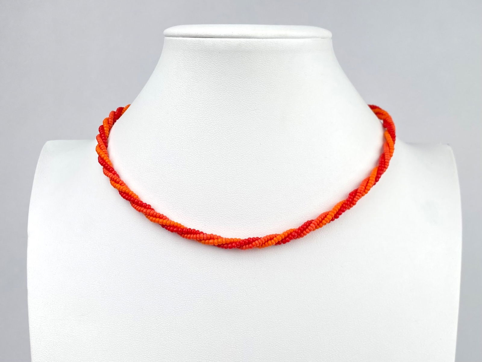 Twisted Red and Orange Beaded Necklace With Metal Clasp: A twisted beaded necklace featuring vibrant red and orange beads, secured with a metallic clasp. The design is made with precision, creating a beautiful twisted pattern with small beads. Necklace is i