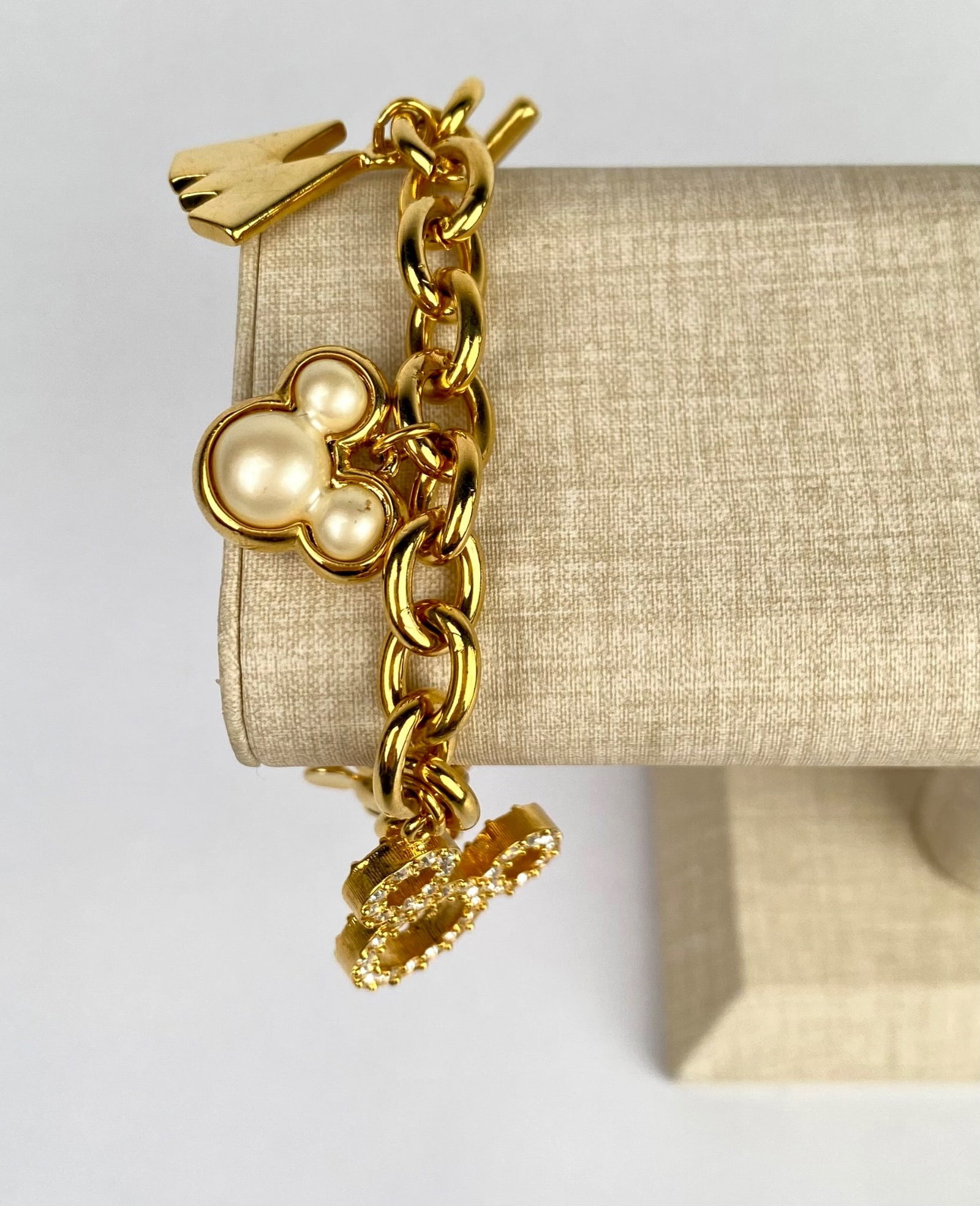 Disney Charm Bracelet with Mickey Mouse and Pearl Accents: Gold plated Disney themed charm bracelet featuring various charms including a crystal encrusted Mickey Mouse, a pearl accented Mickey Mouse silhouette, a gold M engraved with Disney, a dangling single