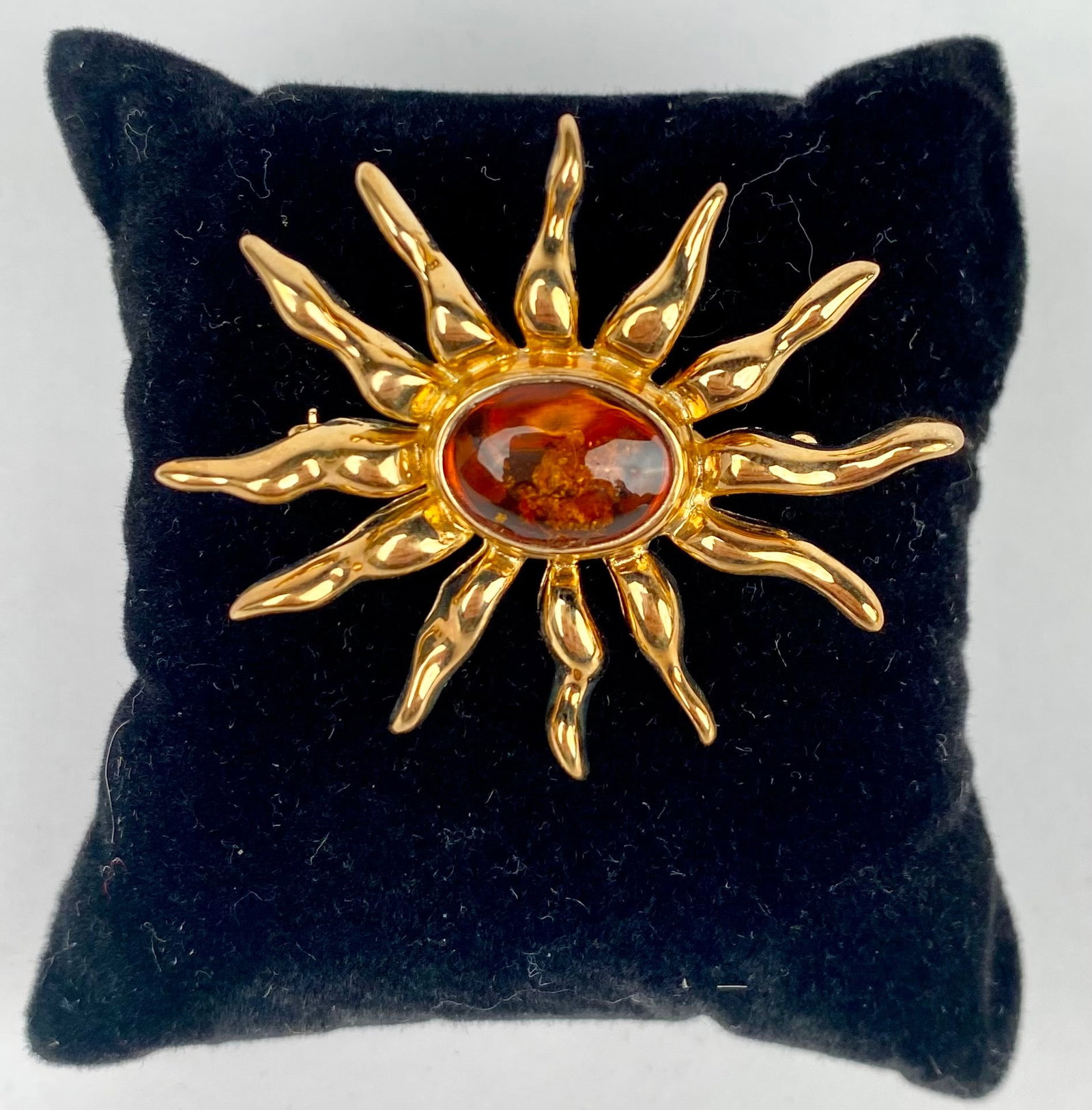 Signed Louis Stern Gold Tone Sunburst Brooch with Amber Center: Gold tone sunburst brooch featuring an oval amber centerpiece with natural inclusions, surrounded by sculpted rays. The reverse includes a secure pin mechanism for attachment and a textured finish. Ha