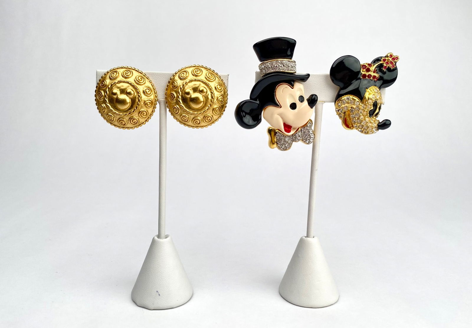 Disney Clip On Earrings and Two Mickey and Minnie Mouse Brooches: A collection of Disney jewelry, including a pair of gold tone clip on earrings with embossed Mickey Mouse patterns, a Minnie Mouse brooch with rhinestone and red enamel accents, and a Mickey Mouse bro