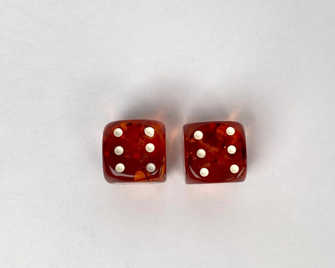 Pair of Mid Century Amber Lucite Dice with Foil Inclusions: Pair of amber lucite dice featuring a translucent appearance with inclusions and white pips. The dice exhibit a warm amber coloration with visible interior details and smooth surfaces. Likely from the
