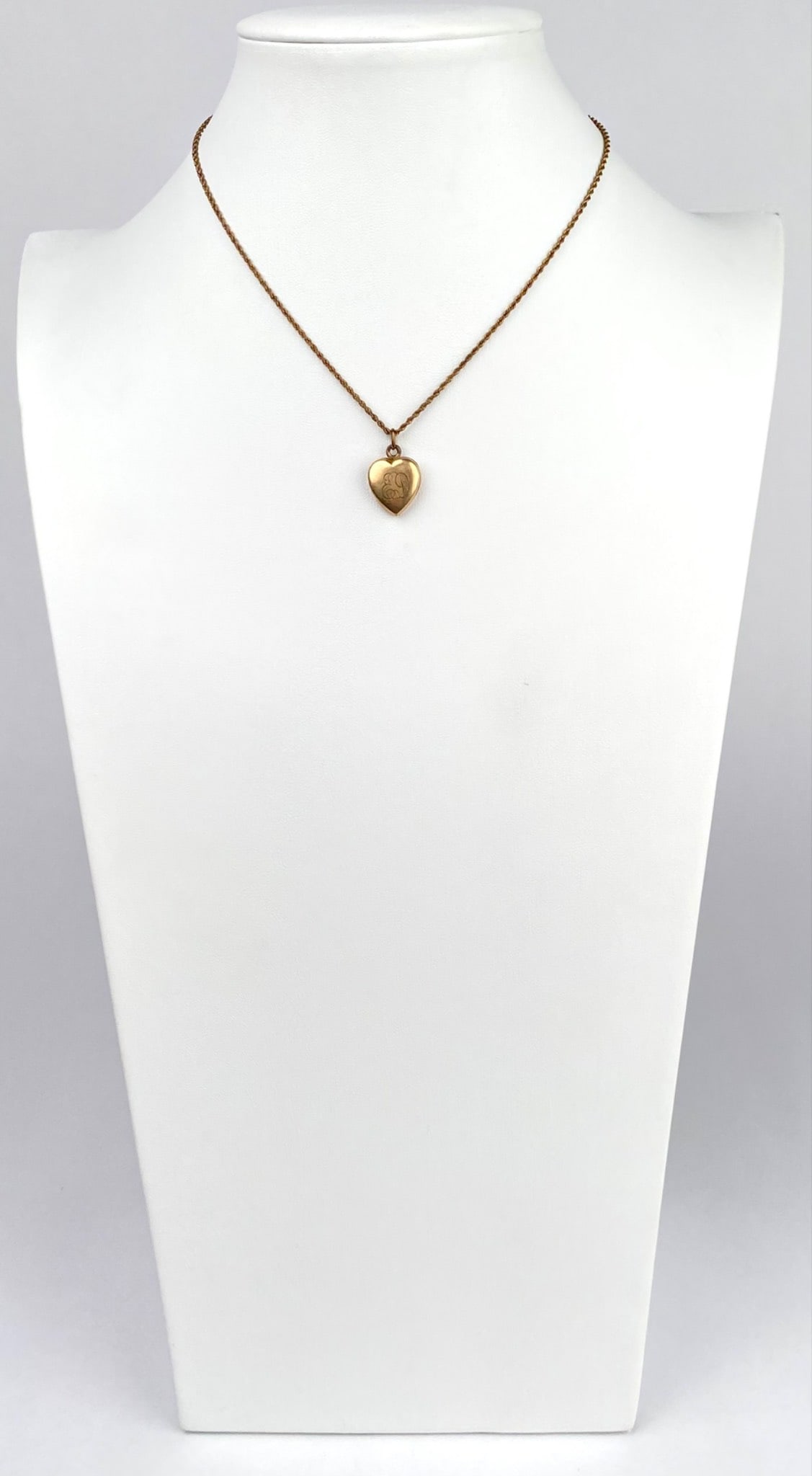 Gold Toned Heart Locket Pendant on Rope Style Chain Necklace: Gold toned heart shaped locket pendant featuring engraved detailing on the front with interior compartments, hanging from a delicate rope style chain necklace. Engraving on the front is ED. The locket