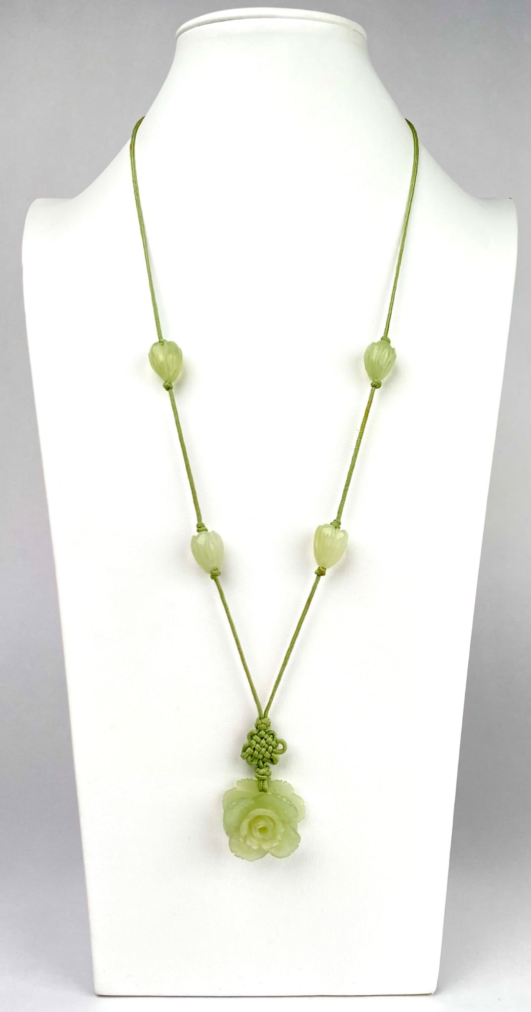Green Necklace With Floral Jade Pendant and Bead Accents: Jade necklace featuring a carved floral shaped pendant in light green, strung on a green cord with multiple bead accents carved into floral shapes. Necklace is in good condition. Please see photos for