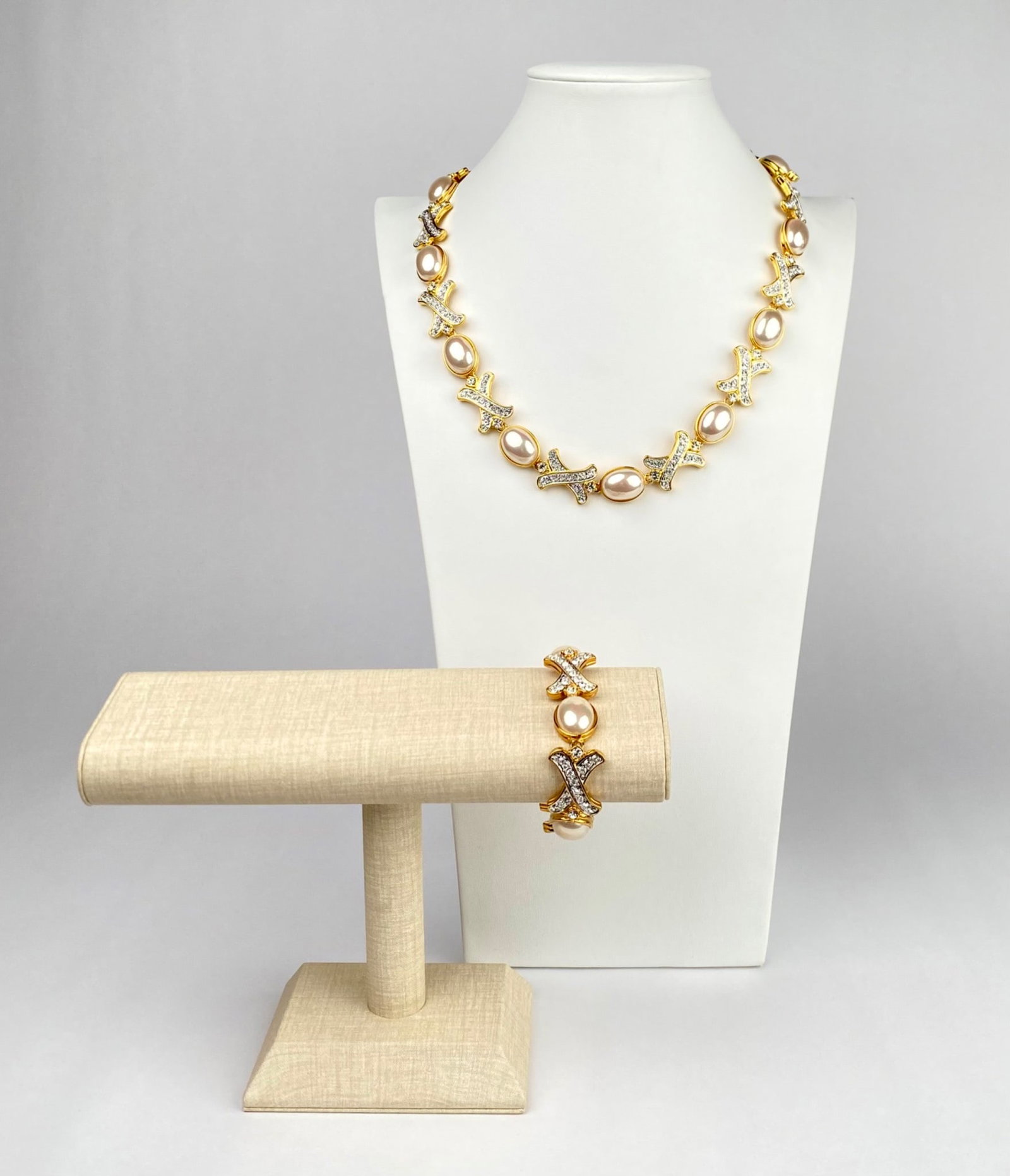 Nolan Miller Gold Tone Necklace and Bracelet Set: Gold tone necklace and bracelet set featuring oval shaped faux pearls and rhinestones Nolan Miller. The necklace and bracelet are designed with alternating X shaped rhinestone patterns and faux pearls