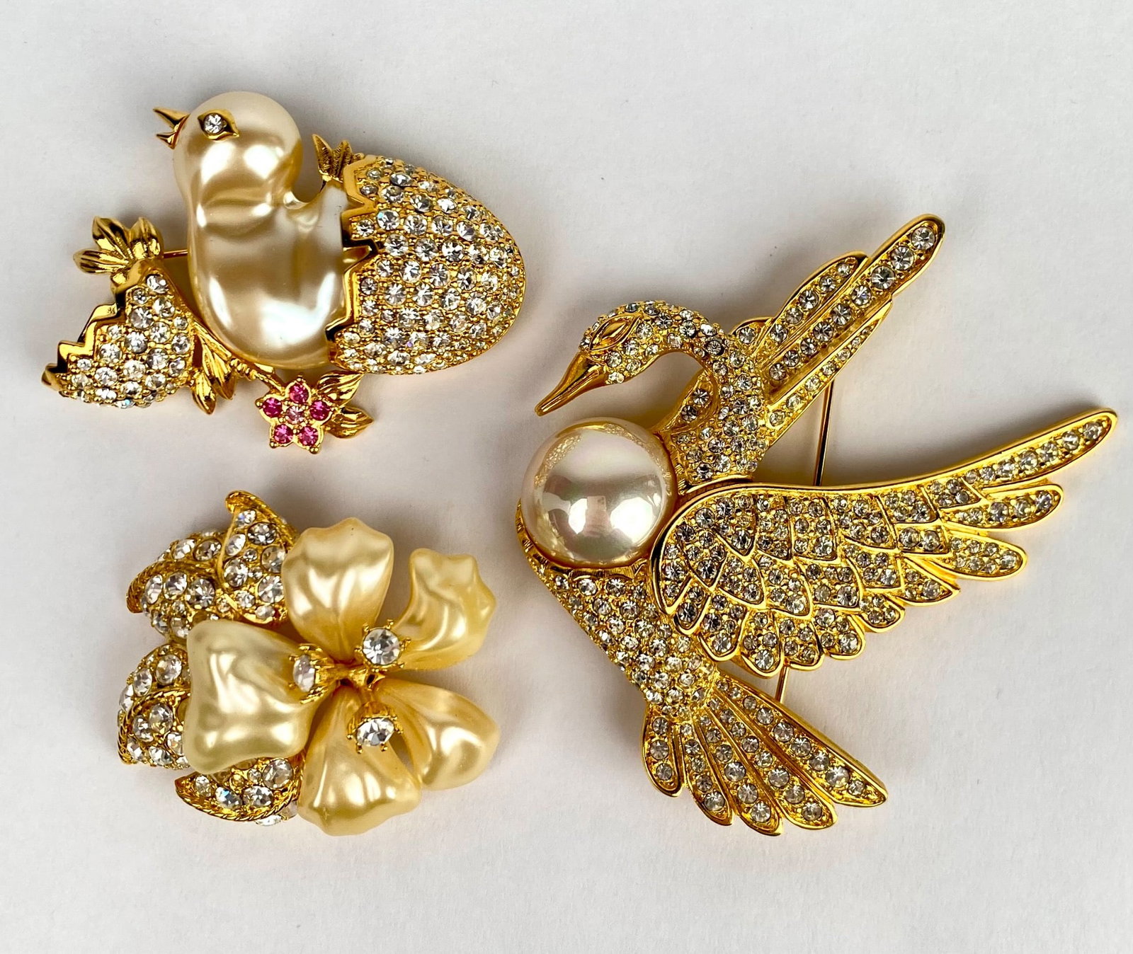 Set of 3 Nolan Miller Brooches with Pearl and Rhinestone Details: Set of 3 Nolan Miller brooches. The set includes a swan with wings adorned with rhinestones and a pearl detail, a chick hatching from a rhinestone egg with pink rhinestone accents, and a floral brooch