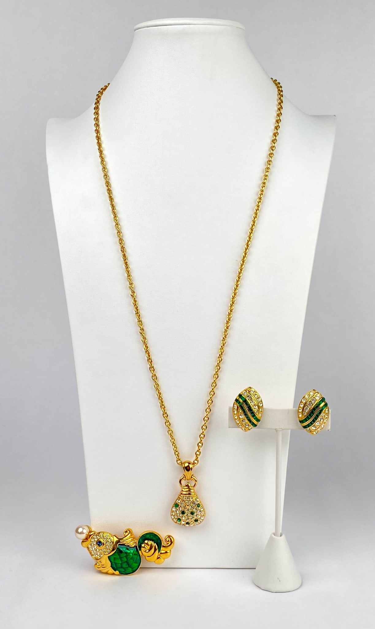 Nolan Miller Gold Tone Necklace Brooch and Clip On Earrings Set: Gold tone jewelry set by Nolan Miller featuring a chain necklace with a teardrop shaped pendant, a brooch in the shape of a fish with green enamel, crystal accents, and a faux pearl, and a pair of cli