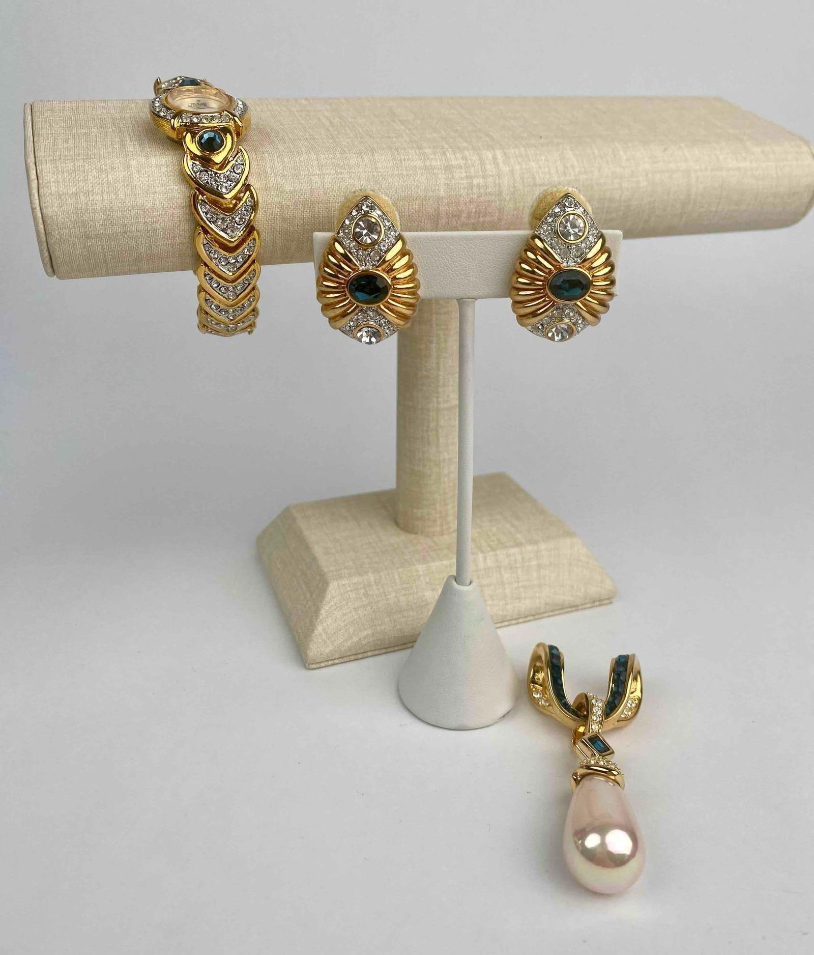 Nolan Miller designer jewelry lot featuring a sparkling quartz wristwatch, coordinating clip-on: Nolan Miller designer jewelry lot featuring a sparkling quartz wristwatch, coordinating clip-on earrings, and a large pendant. The gold-tone watch showcases a mother-of-pearl face surrounded by clear