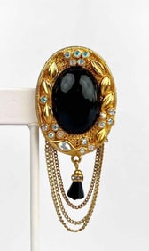 Gold tone framed brooch with black oval glass by K.J.L. Brooch has chain and hanging bead details.