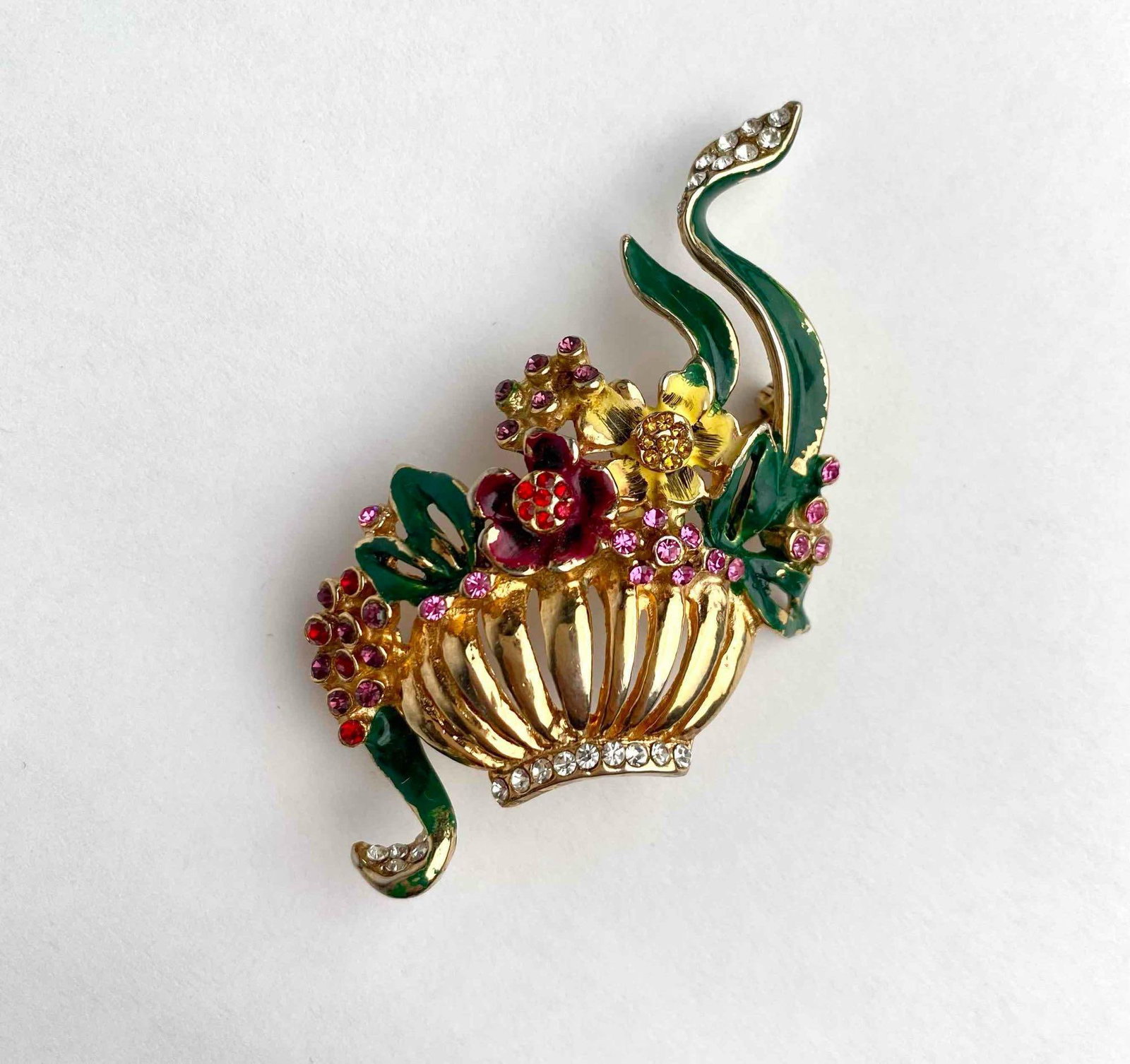 Gold tone flower pot brooch. Brooch is a pot with flowers and vines flowing out of it with colored: Gold tone flower pot brooch. Brooch is a pot with flowers and vines flowing out of it with colored rhinestone details. Wear and flaking is noticeable on the brooch and is consistent with age and use. 