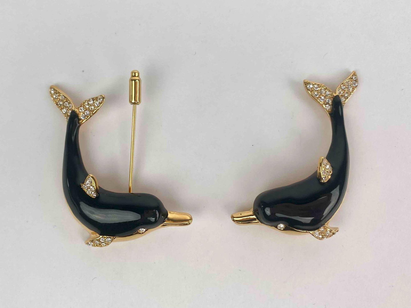 Pair of signed KJL (Kenneth Jay Lane) dolphin brooches featuring glossy black enamel bodies and: Pair of signed KJL (Kenneth Jay Lane) dolphin brooches featuring glossy black enamel bodies and gold tone detailing. Each dolphin is adorned with clear crystal accents on the fins, tails and eyes for 