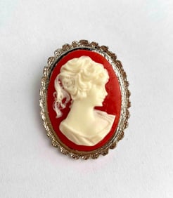 A vintage costume cameo brooch featuring a high relief white female bust set against a vibrant red