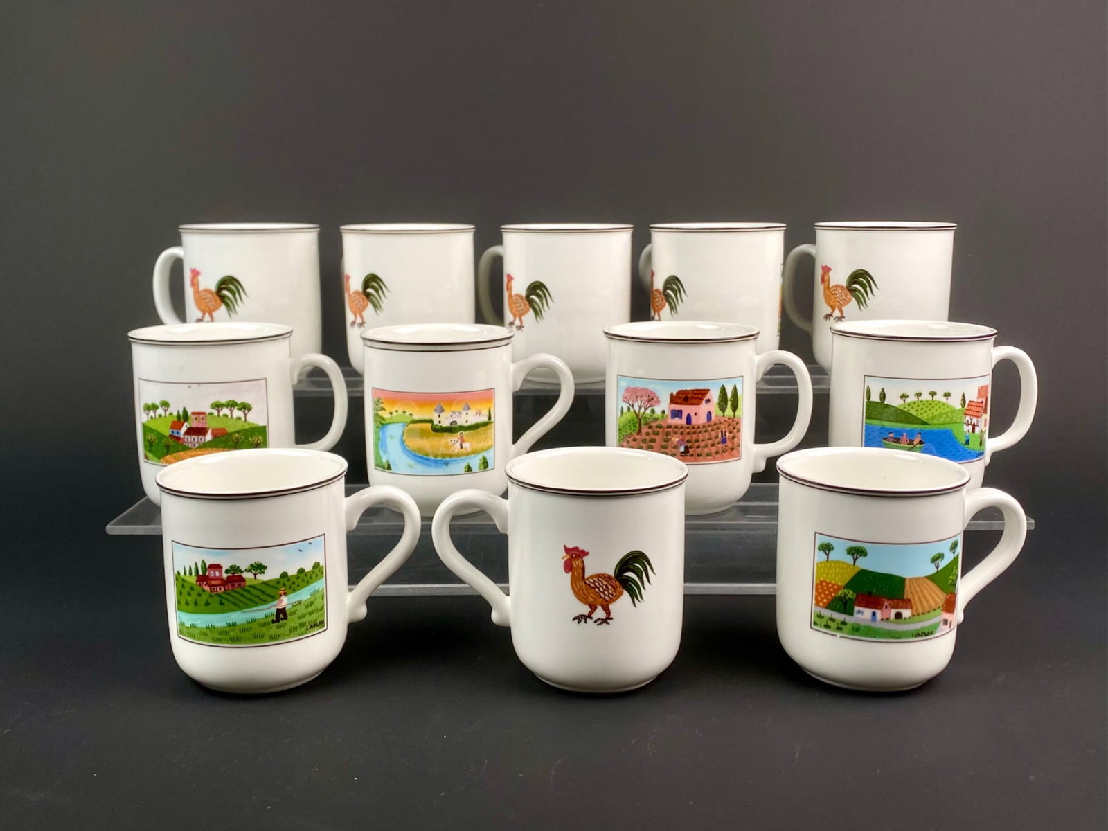 Set of 12 Villeroy & Boch Design Naif Porcelain Mugs: Set of twelve porcelain mugs from Villeroy and Boch's Design Naif series featuring artwork by Gerard Laplau. Each mug showcases a rural or village scene in folk art style, including pastoral landscape