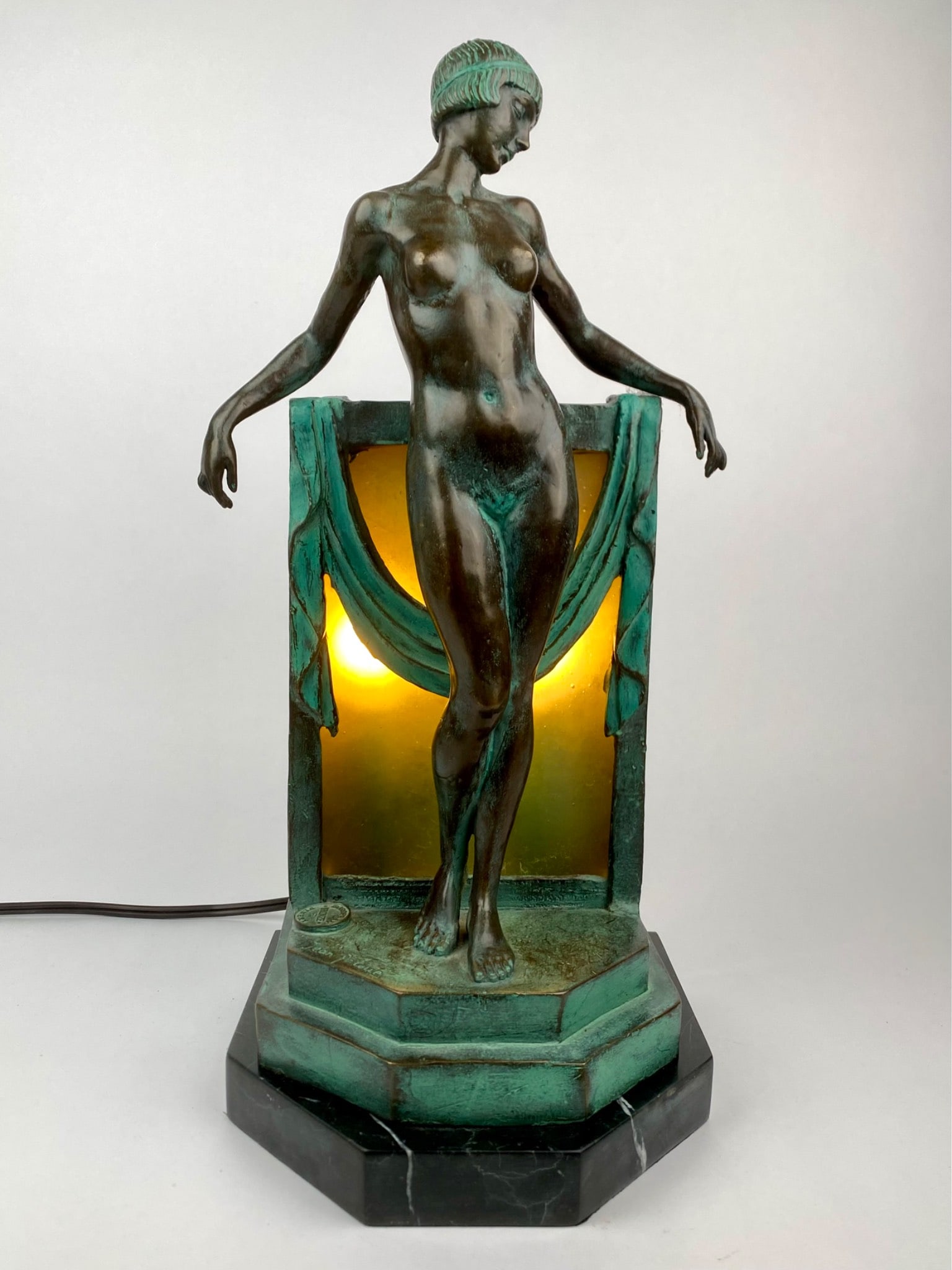 Art Deco Style Bronze Nude Figural Lamp Signed Jean Patoue: Art Deco style figural lamp featuring a nude female figure cast in bronze with a patinated finish. The figure is mounted on a stepped octagonal black marble base and illuminated from behind with a fro