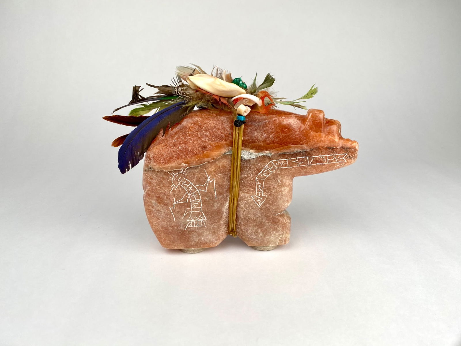 Zuni Style Handcrafted Stone Fetish Bear with Offering Bundle: Handcrafted stone fetish bear adorned with etched designs on both sides, featuring depictions resembling symbolic figures and directional arrows. The bear is accented with decorative elements, includi