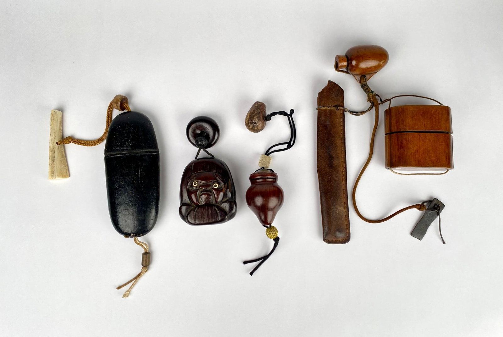Japanese Inro, Netsuke, and Ojime with Accessories: Japanese inro, netsuke, and ojime, including a wooden inro with a gourd shaped stopper, a lacquered inro with bone toggle, and a carved wood netsuke with inset eyes. The set also includes a leather po