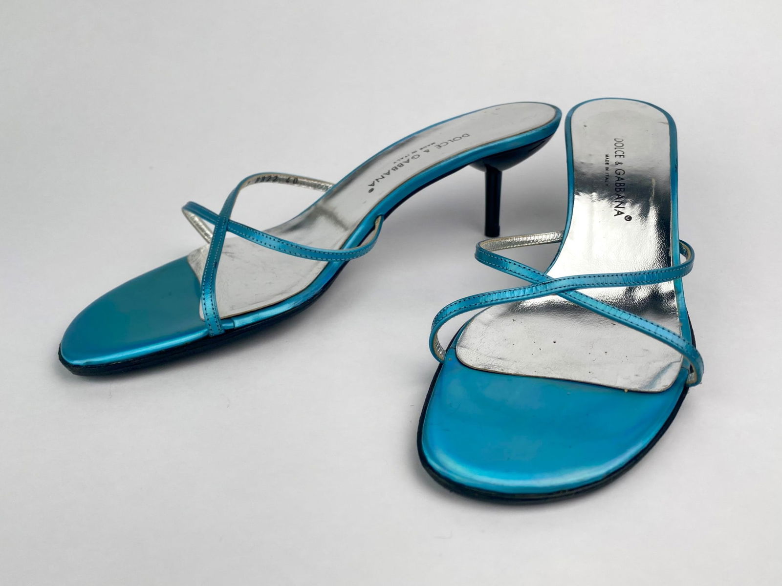 Dolce & Gabbana Blue Metallic Strappy Heeled Sandals (Size 40): Pair of Dolce & Gabbana strappy heeled sandals in a metallic blue finish with silver insoles. The sandals feature slim crossover straps and a sleek black heel. Marked "Dolce & Gabbana Mad