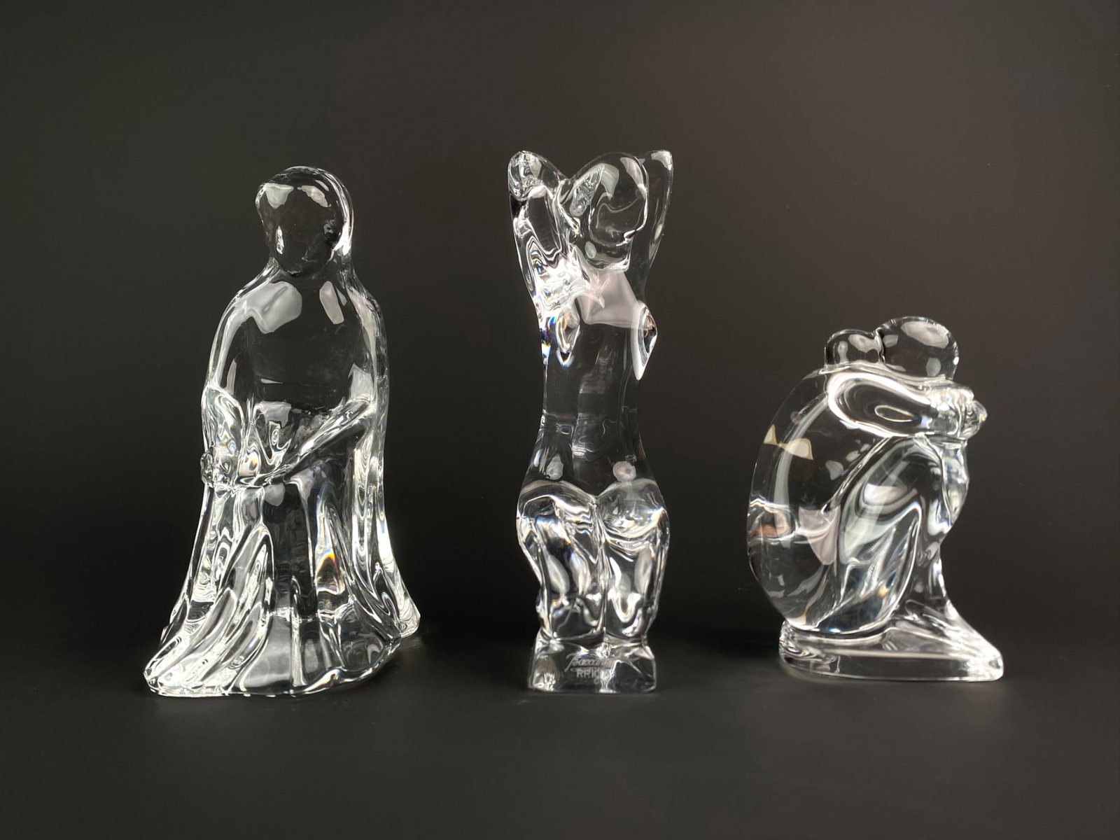 Set of Three Signed Baccarat Crystal Female Figurines: Set of three clear lead crystal art glass figurines by Baccarat, France, each depicting a stylized female figure in various contemplative or dynamic poses. The base of each is singed Baccarat featurin