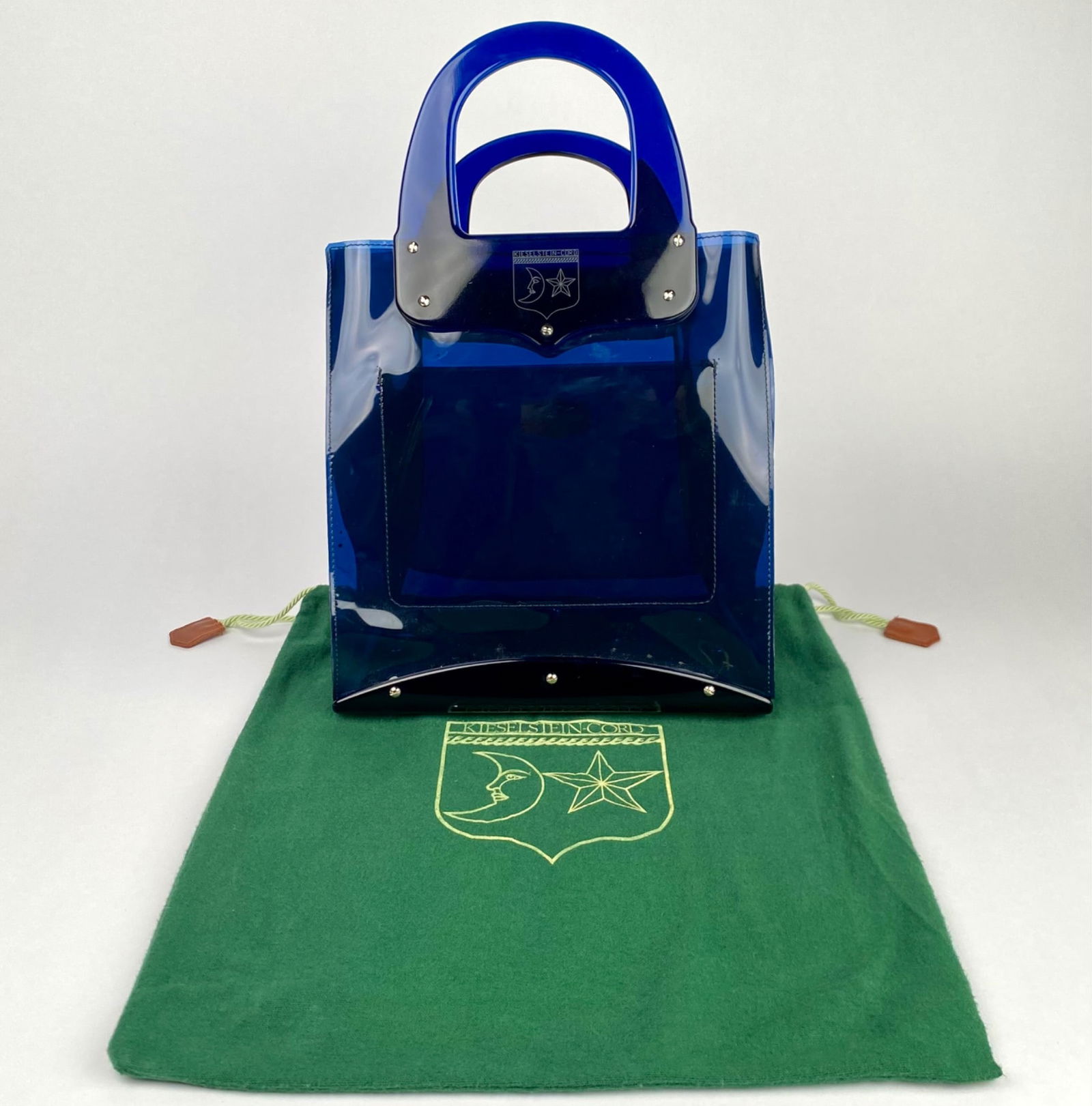 Kieselstein Cord Midnight Blue Lucite Handbag with Dust Bag: Blue transparent handbag featuring a moon and star crest engraved on the front plate. This bag comes with silver tone hardware and a matching green logo emblazoned drawstring dust bag. Handbag is in g