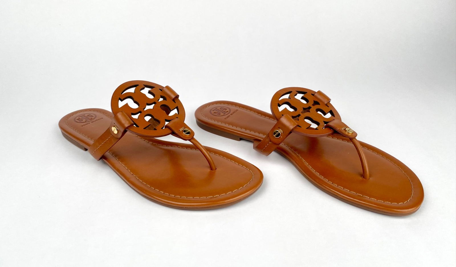 Tory Burch Miller Sandals in Tan Leather (Size 10): Tory Burch Miller sandals crafted in tan leather with the double T medallion detail at the toe. These sandals feature a cushioned footbed and rubber soles with embossed branding. Size marked as 10. Sa