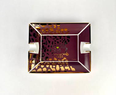 Cartier Porcelain Ashtray with Swarovski Crystal Details (5 x 7): Cartier ceramic ashtray adorned with an intricate panther motif in gold and black on a deep maroon background. The ashtray features gold trim along the edges and two cigarette rests. The base is cover