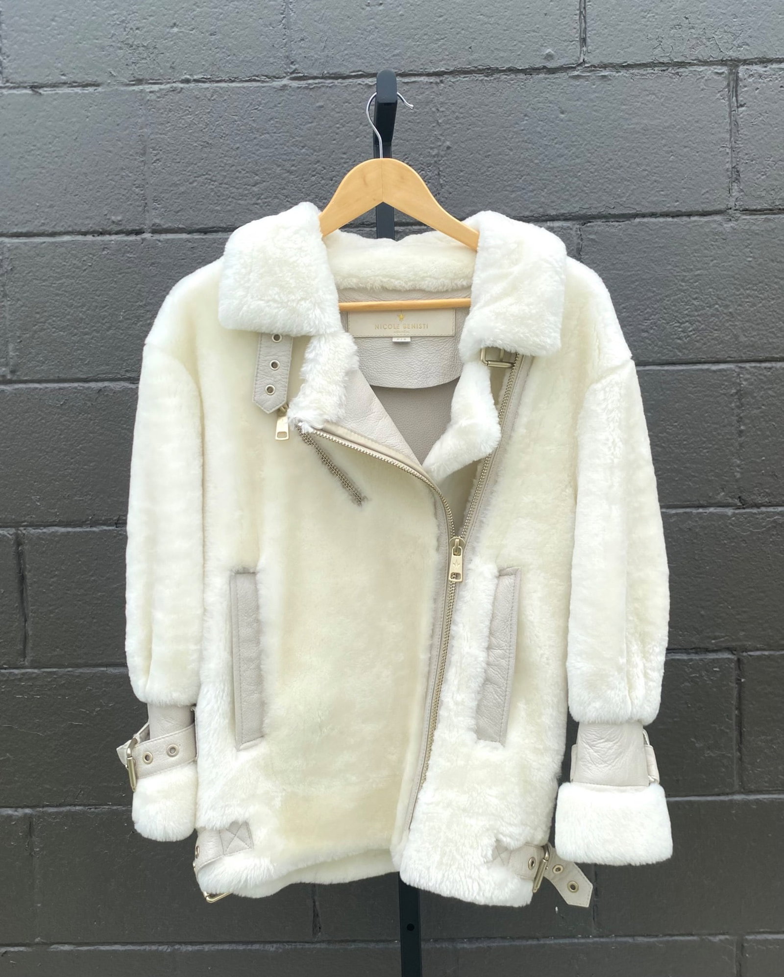 Nicole Benisti Shearling Aviator Jacket in Ivory (Size P/S): Nicole Benisti shearling aviator style jacket in ivory, featuring gold tone hardware accents. Details include buckle closure accents on cuffs and hem, asymmetrical zip front, and leather lined interio