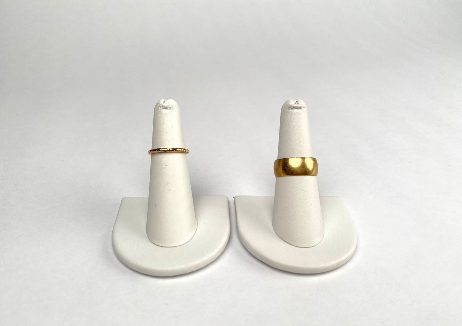 Two Gold Rings Marked 10K and 14K: Two gold rings, one marked 10K with a smooth finish and the other marked 14K featuring an engraved design. Both rings show signs of wear consistent with age and use. Both rings have stamps and hallmar