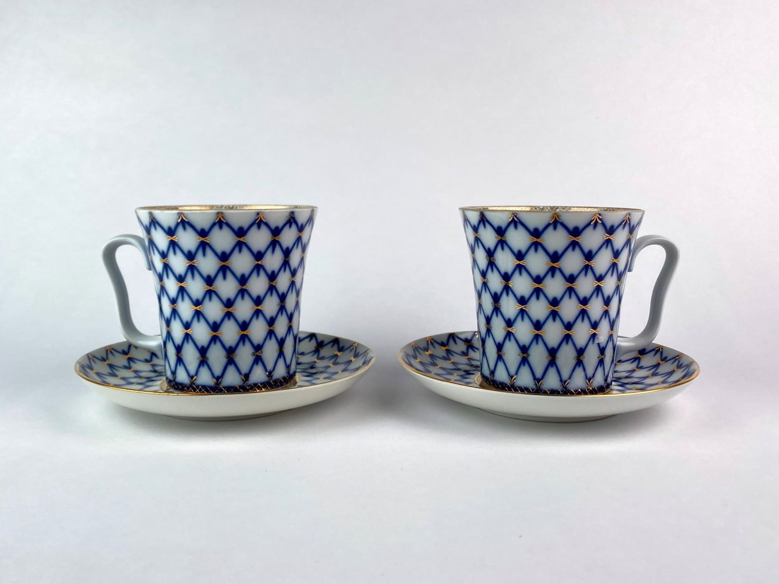 Pair of Lomonosov Imperial Porcelain Cobalt Net Mugs and Saucers: Pair of Lomonosov Imperial Porcelain Factory coffee mugs with matching saucers, featuring the factory's iconic Cobalt Net pattern. The white porcelain ground is hand decorated with cobalt blue lat