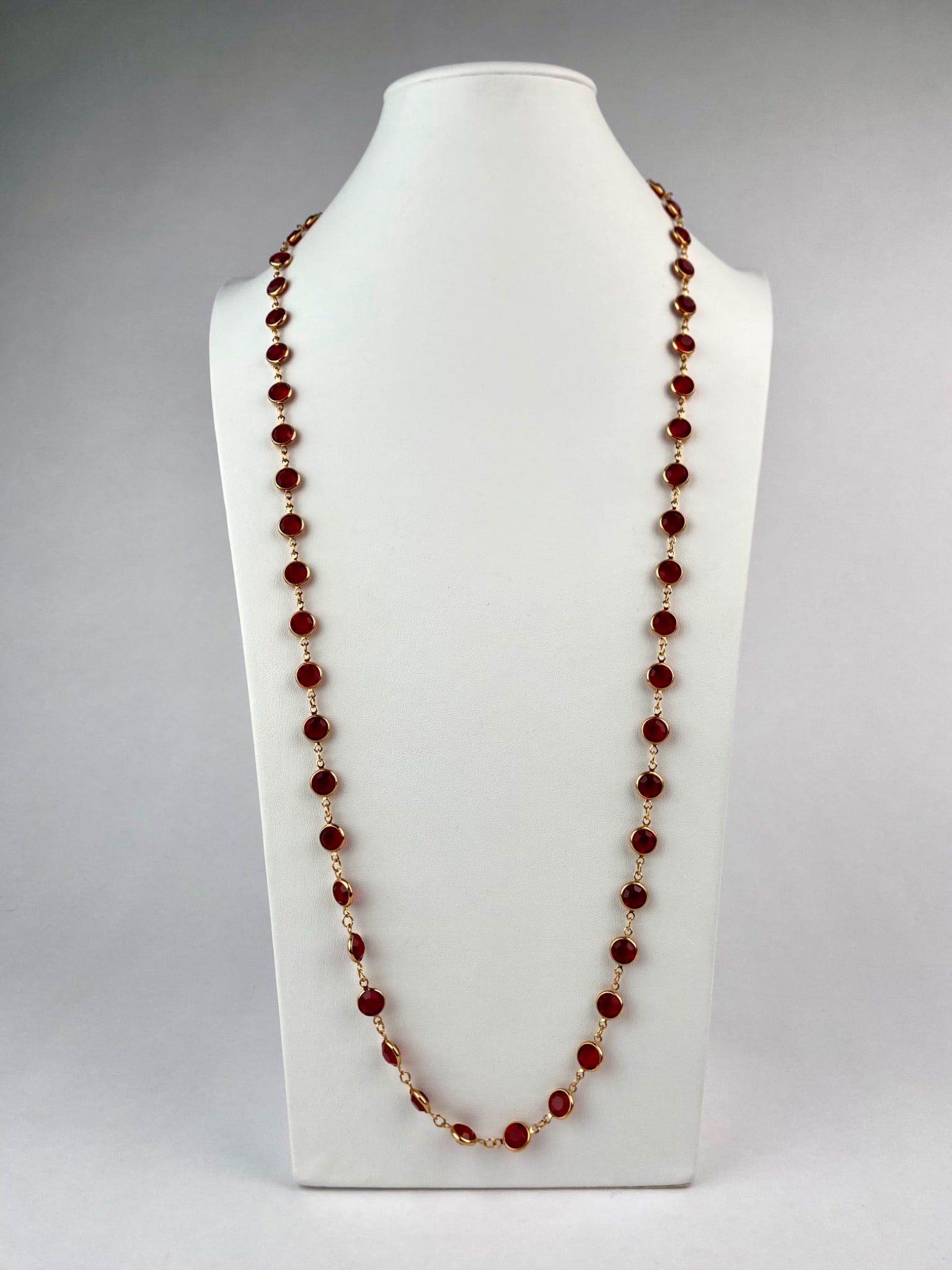 Swarovski Faceted Red Crystal Station Necklace: Long Swarovski station necklace featuring round faceted red crystals bezel-set in gold-tone metal. The design allows it to be worn as a single strand or doubled for a layered look. The necklace is mar
