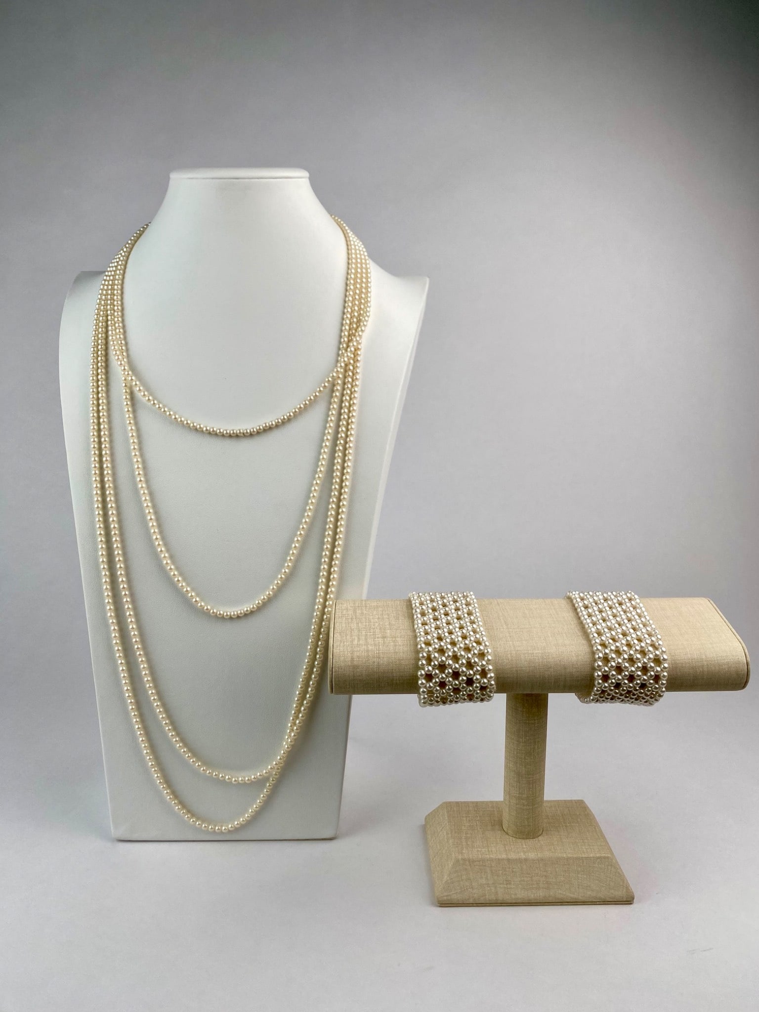 Long Faux Pearl Necklace with Wide Faux Pearl Cuff Bracelets: Classic costume jewelry set featuring a long single strand of faux pearls and a pair of wide faux pearl cuff bracelets. The necklace is shown wrapped multiple times to create a layered look. The simul