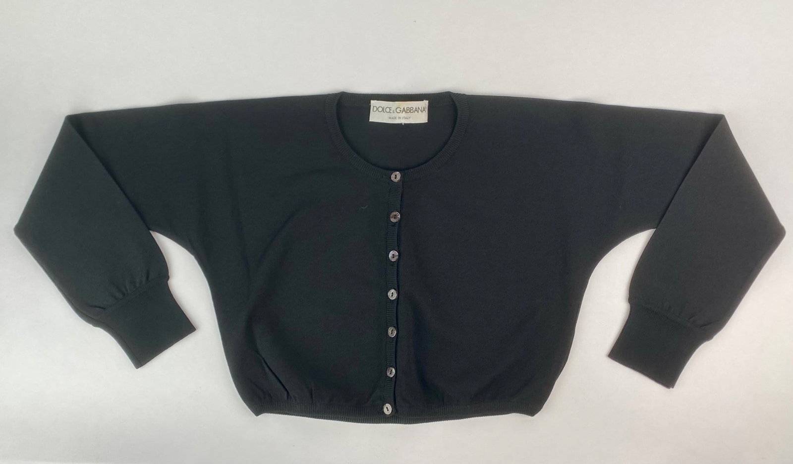 Dolce & Gabbana Black Long Sleeve Cropped Knit Cardigan: Dolce and Gabbana black cropped cardigan with long sleeves and a classic button front closure. The buttons feature iridescent branding, and the rib-knit trim adds structure to the collar, cuffs, and h