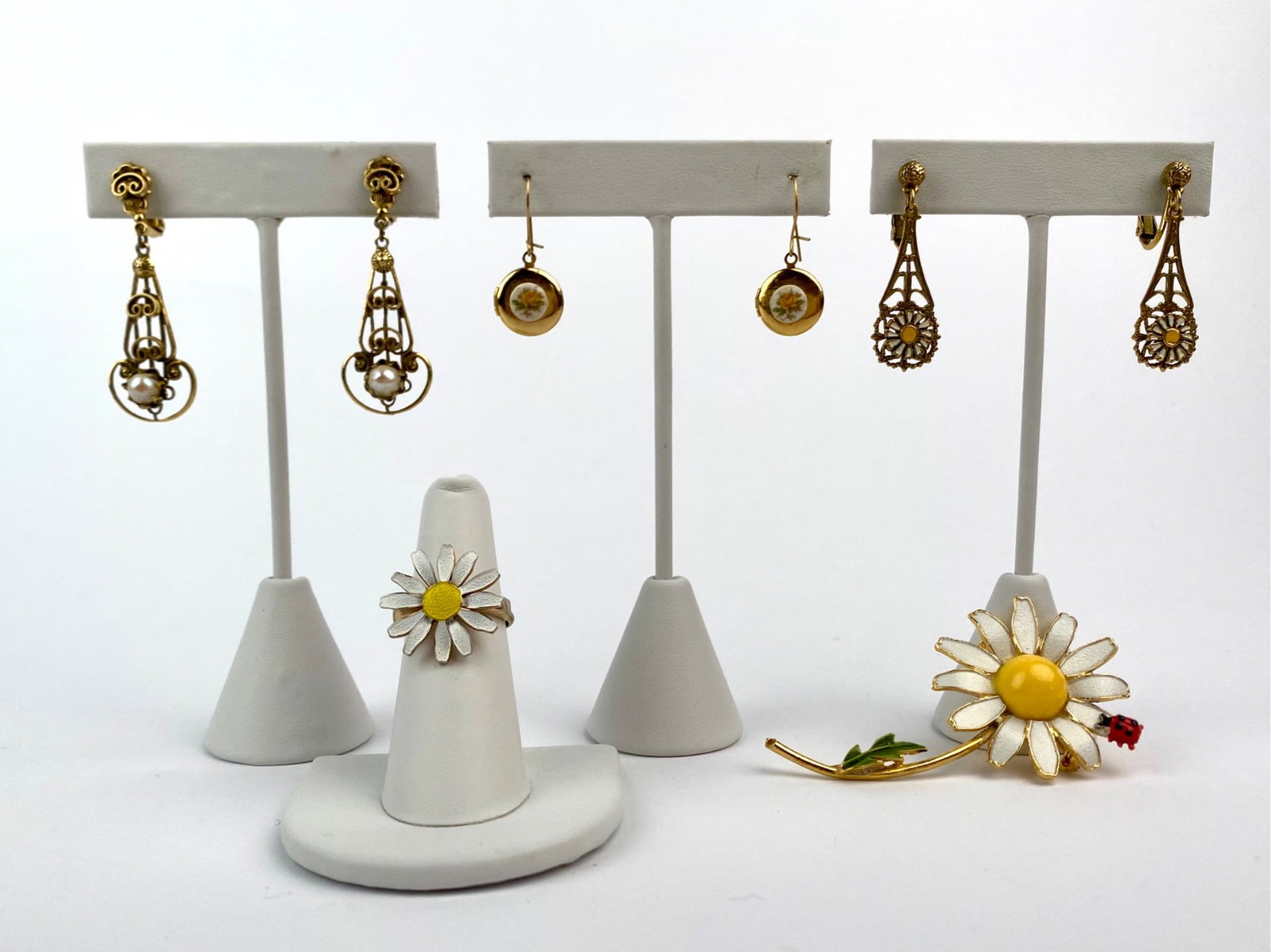 Group of Daisy-Themed and Gold-Tone Costume Jewelry: Group of vintage daisy themed and gold-tone costume jewelry. The lot includes one pair of gold-tone clip on drop earrings with filigree and faux pearl accents, a pair of gold-tone locket-style earring