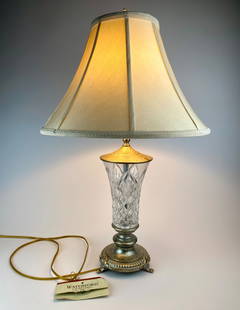 Waterford Crystal and Antiqued Brass Table Lamp with Shade: Waterford crystal table lamp featuring a cut crystal vase-form body set into an ornate antiqued brass-tone base with paw feet and foliate detailing. The lamp includes its original cream-colored fabric