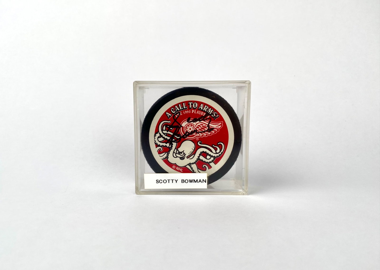 1995 NHL Playoffs A Call to Arms Puck Signed by Scotty Bowman: 1995 NHL Playoffs ‘A Call to Arms’ hockey puck, officially licensed by NHL and manufactured by Trench Manufacturing. Features a red and white Detroit Red Wings design with an octopus motif. Signed