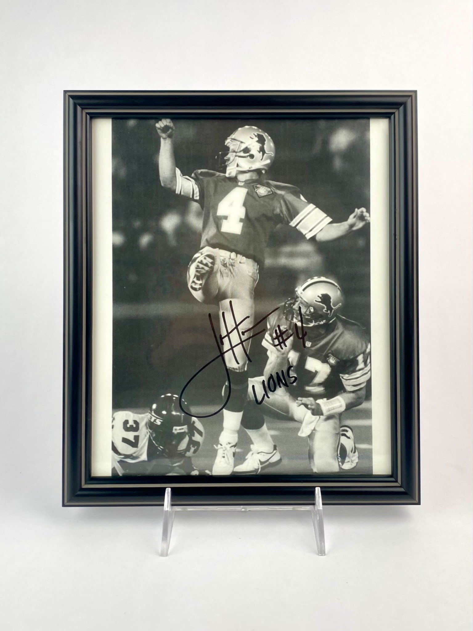 Framed Jason Hanson Signed Detroit Lions Photo: Framed black and white action photograph of Jason Hanson, long-tie placekicker for the Detroit Lions. It is hand-signed in bold black marker with the inscription "#4 Lions." The photo is professionall